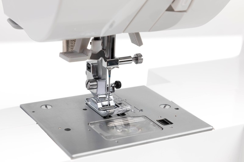 Detail einer weißen Nähmaschine, Nadel und Fußplatte auf weißem Hintergrund.
