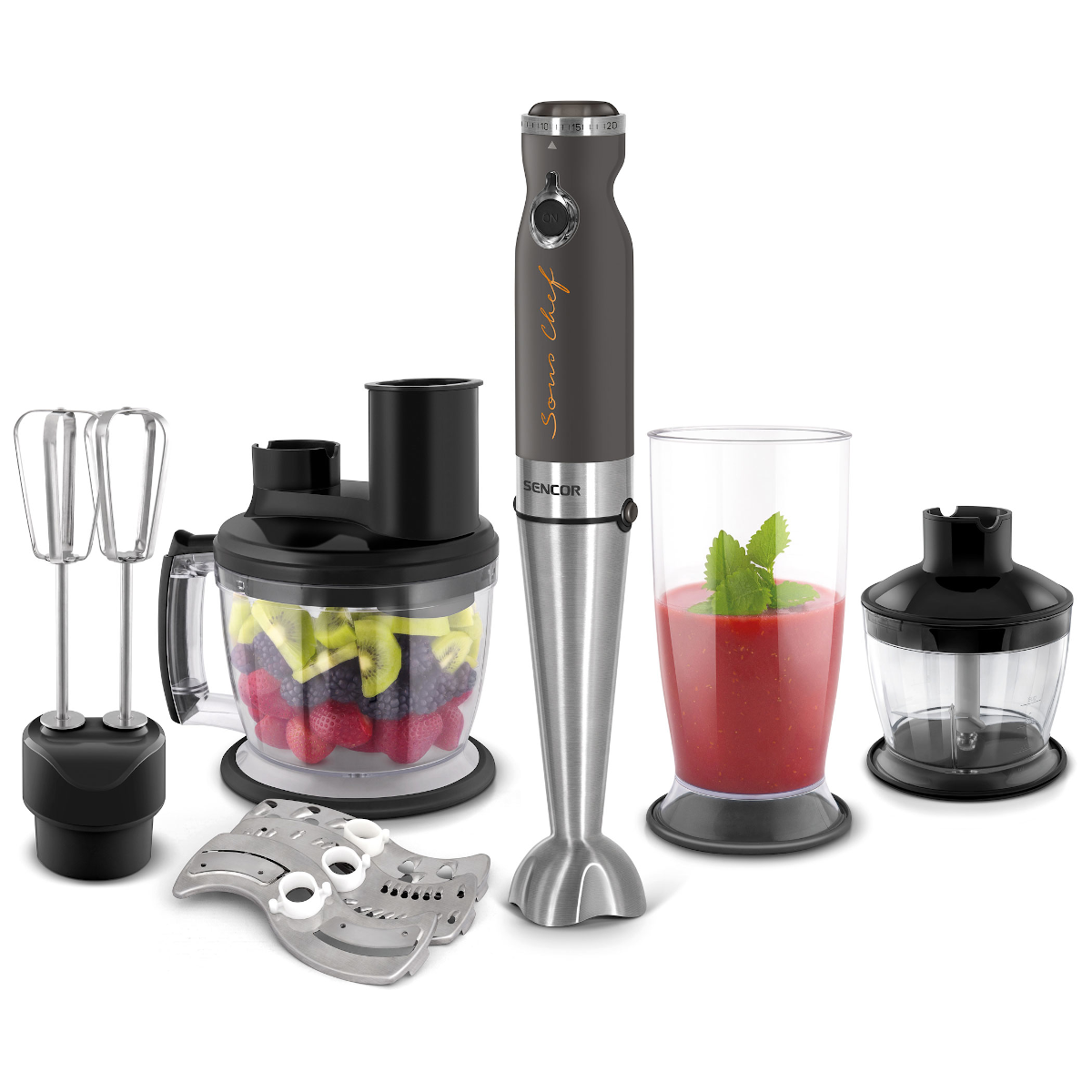 Kézi mixer tartozékokkal: habverő, aprító, penge és egy pohár vörös keverékkel. Fehér háttér.