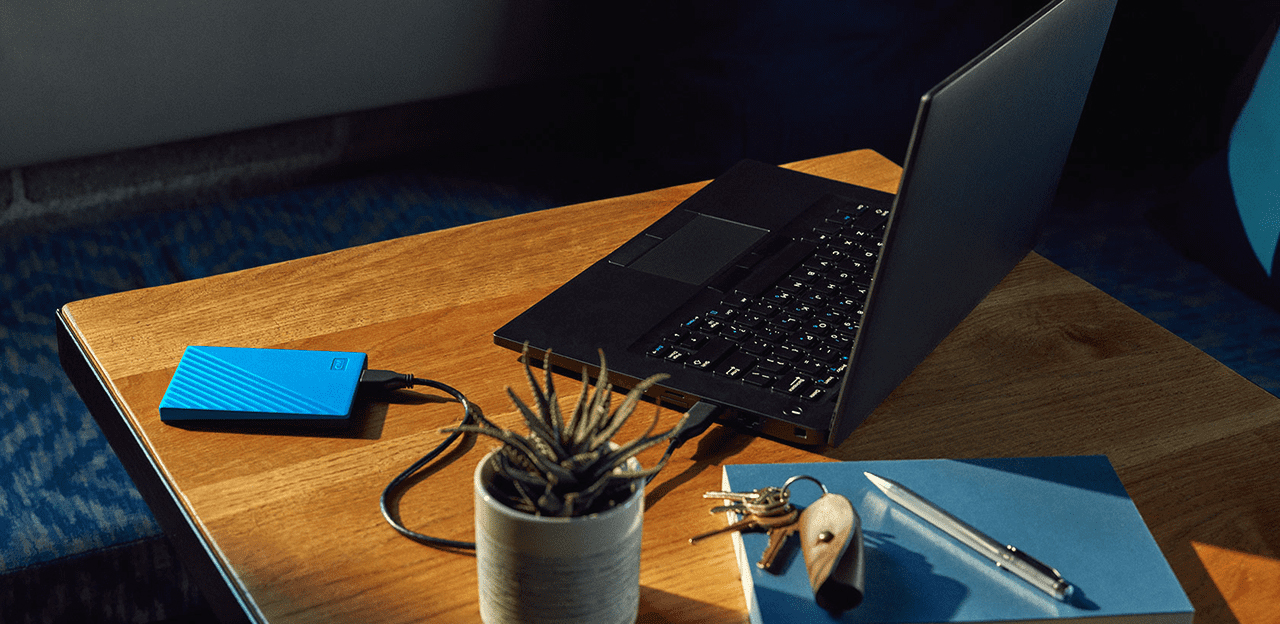 Un ordinateur portable noir et un disque dur bleu sont sur une table en bois.