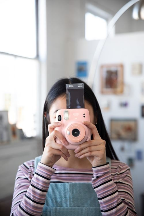 Una persona sosteniendo una cámara Instax rosa. La cámara está apuntando al espectador.