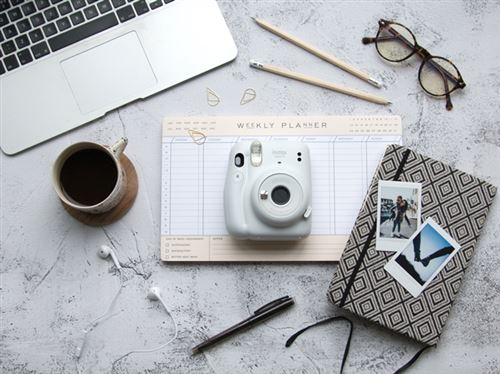 Escritorio con laptop, cámara, bolígrafos, gafas, café, cuaderno y planificador semanal.