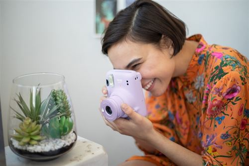 Mujer sonriendo, sosteniendo una cámara Instax morada y mirando el visor.