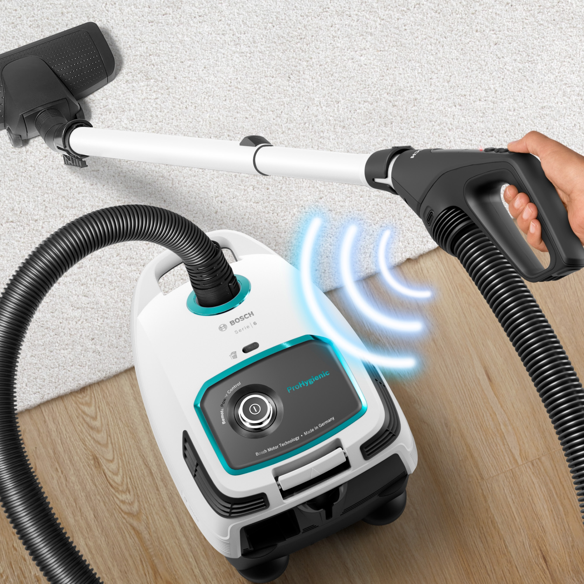 Weißer Bosch-Staubsauger auf Teppich. Eine Hand hält den Schlauch. Blaue Energiewellen-Grafiken werden gezeigt.