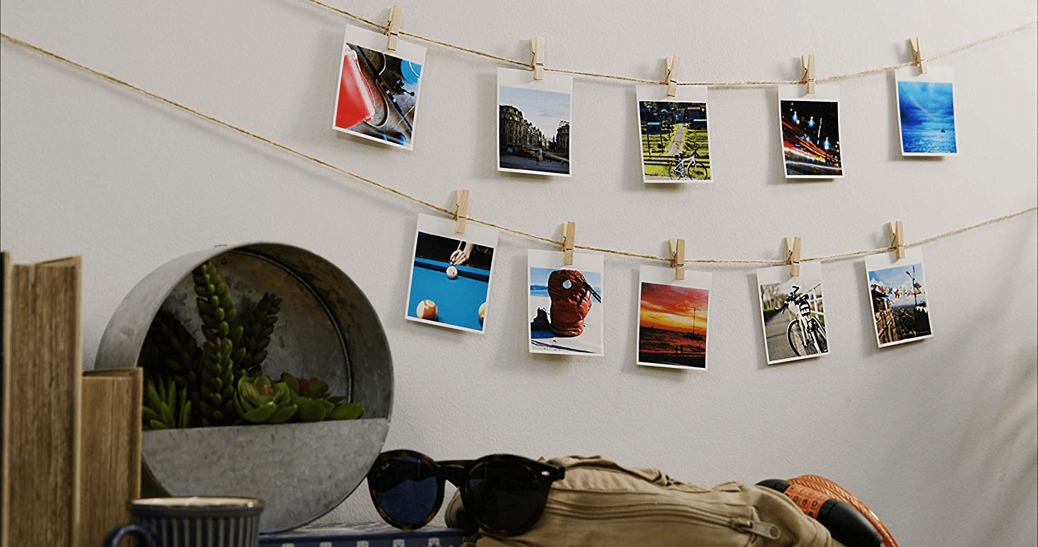 Photos accrochées à une ficelle sur un mur. Succulentes dans un pot en métal, lunettes de soleil, sac à dos et tasse au premier plan.