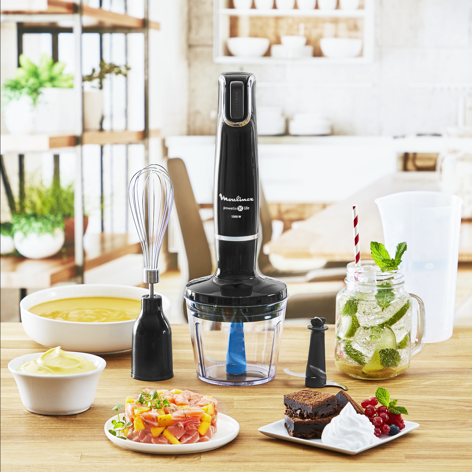 Black hand blender with accessories and various foods on a wooden table.