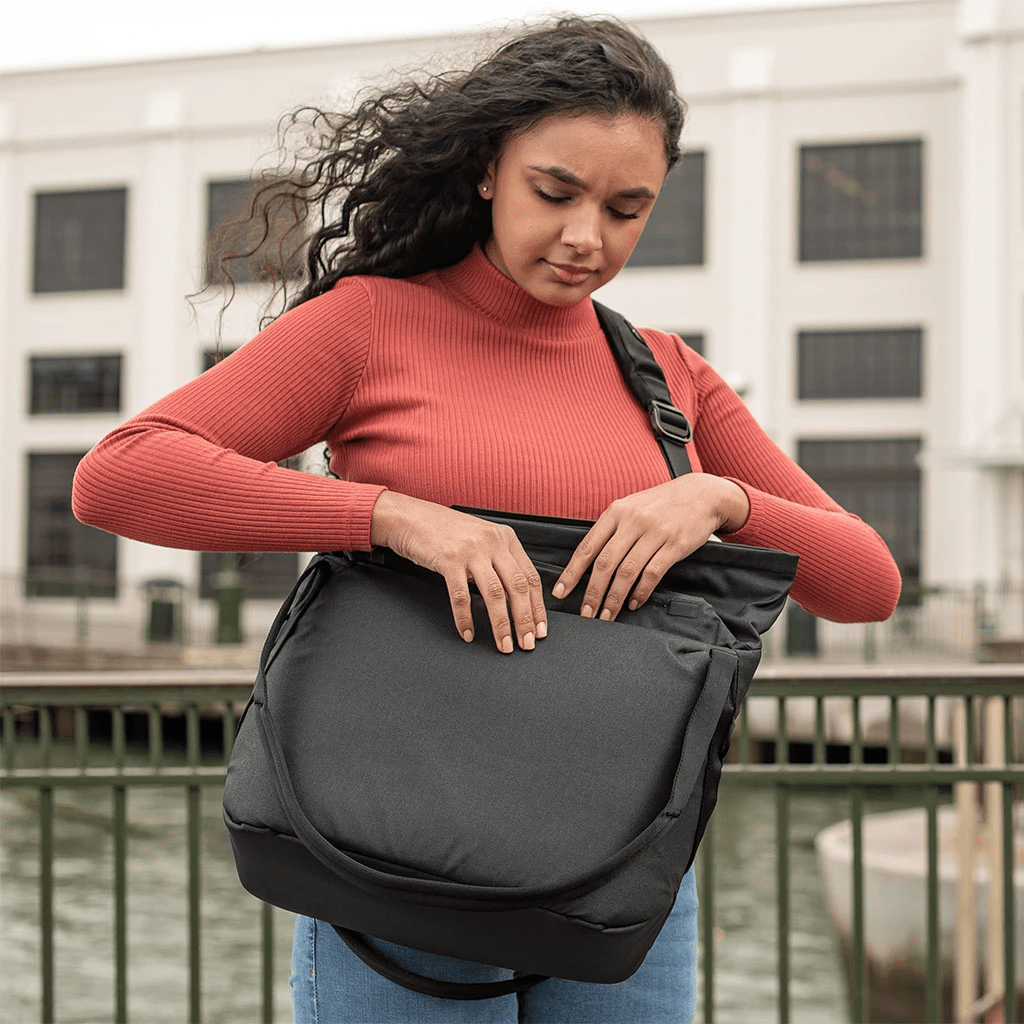 Donna con top rosso apre una borsa nera. Lo sfondo mostra un edificio e acqua. Lei è fuori.