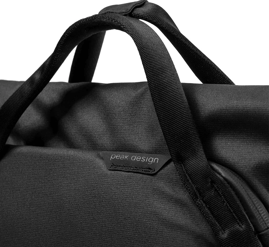 Primo piano di una borsa nera con manici. Il logo Peak Design è visibile. La borsa è in tessuto strutturato.