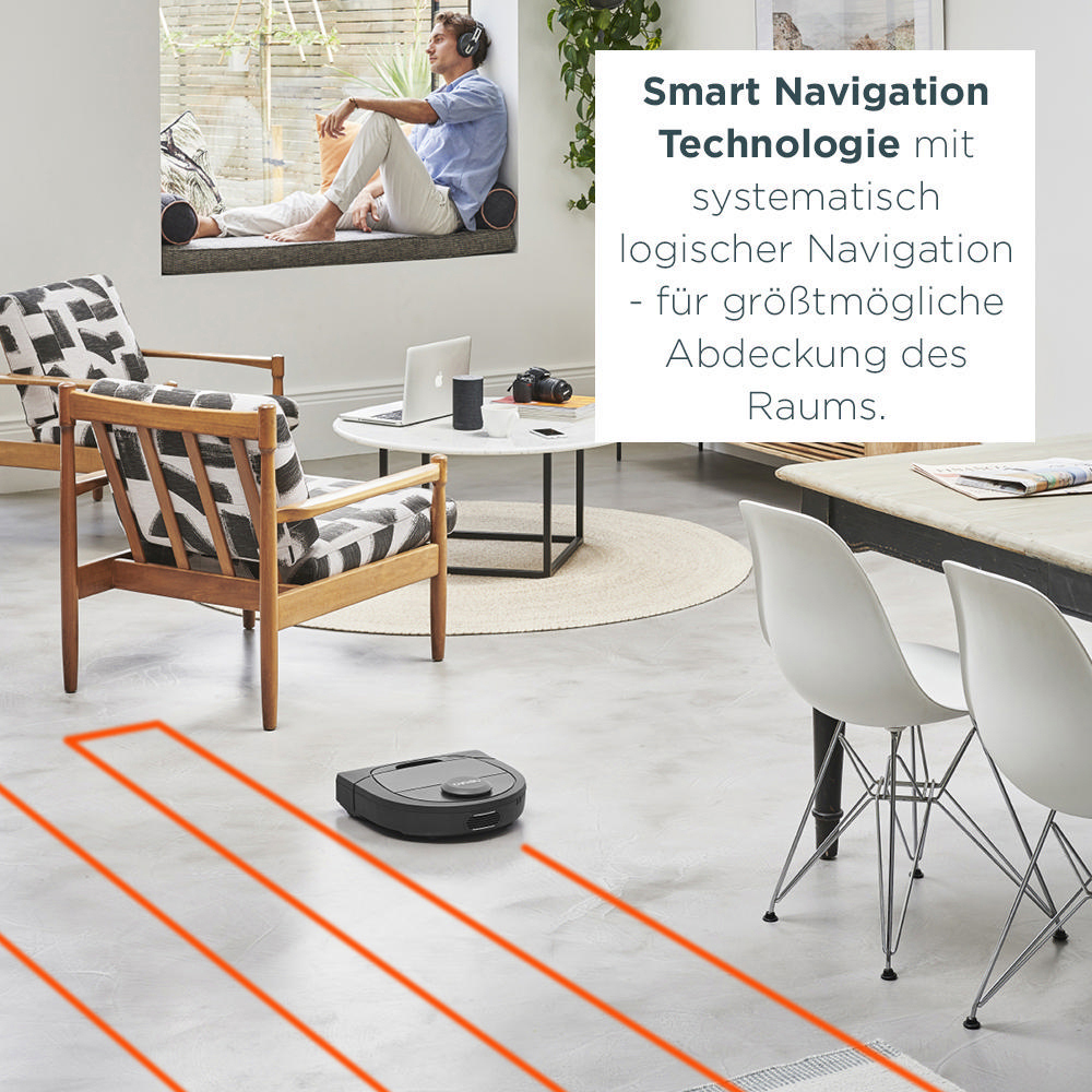 Ein Mann sitzt am Fenster. Ein Roboterstaubsauger reinigt einen Raum. Stühle, Tisch und Teppich sind sichtbar.