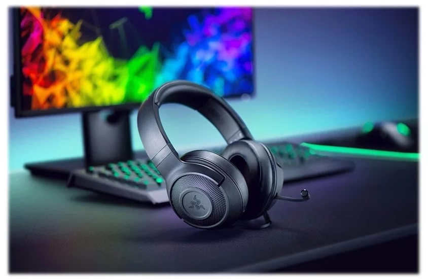 Schwarze Gaming-Kopfhörer auf einem Schreibtisch mit Monitor und Tastatur im Hintergrund.