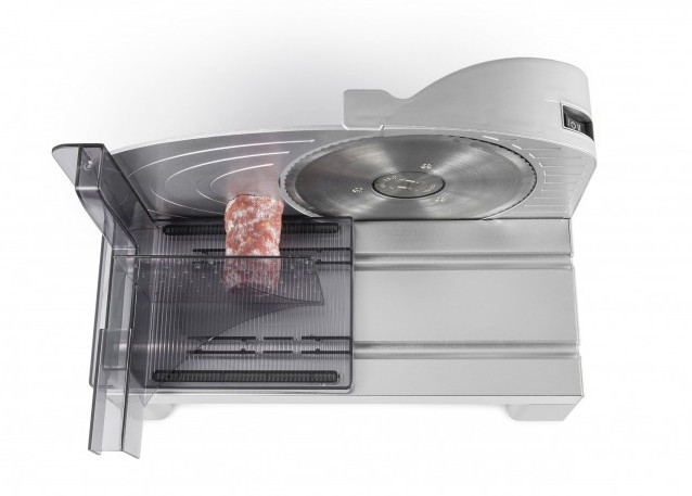 Meat slicer with a sausage in the tray, on a white surface, angled view.