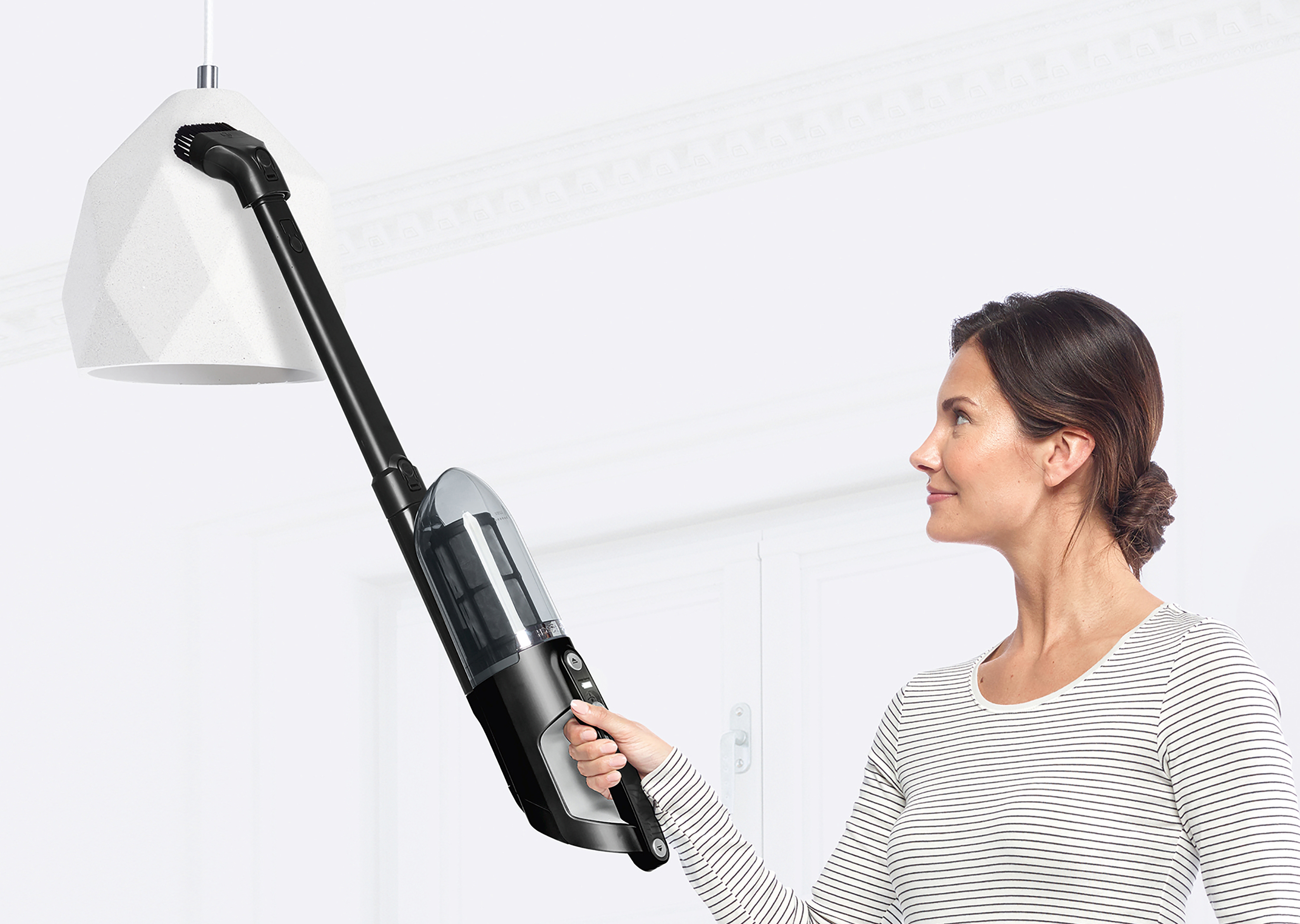 Frau, die eine weiße Lampe mit einem schwarzen und silbernen Handstaubsauger absaugt.