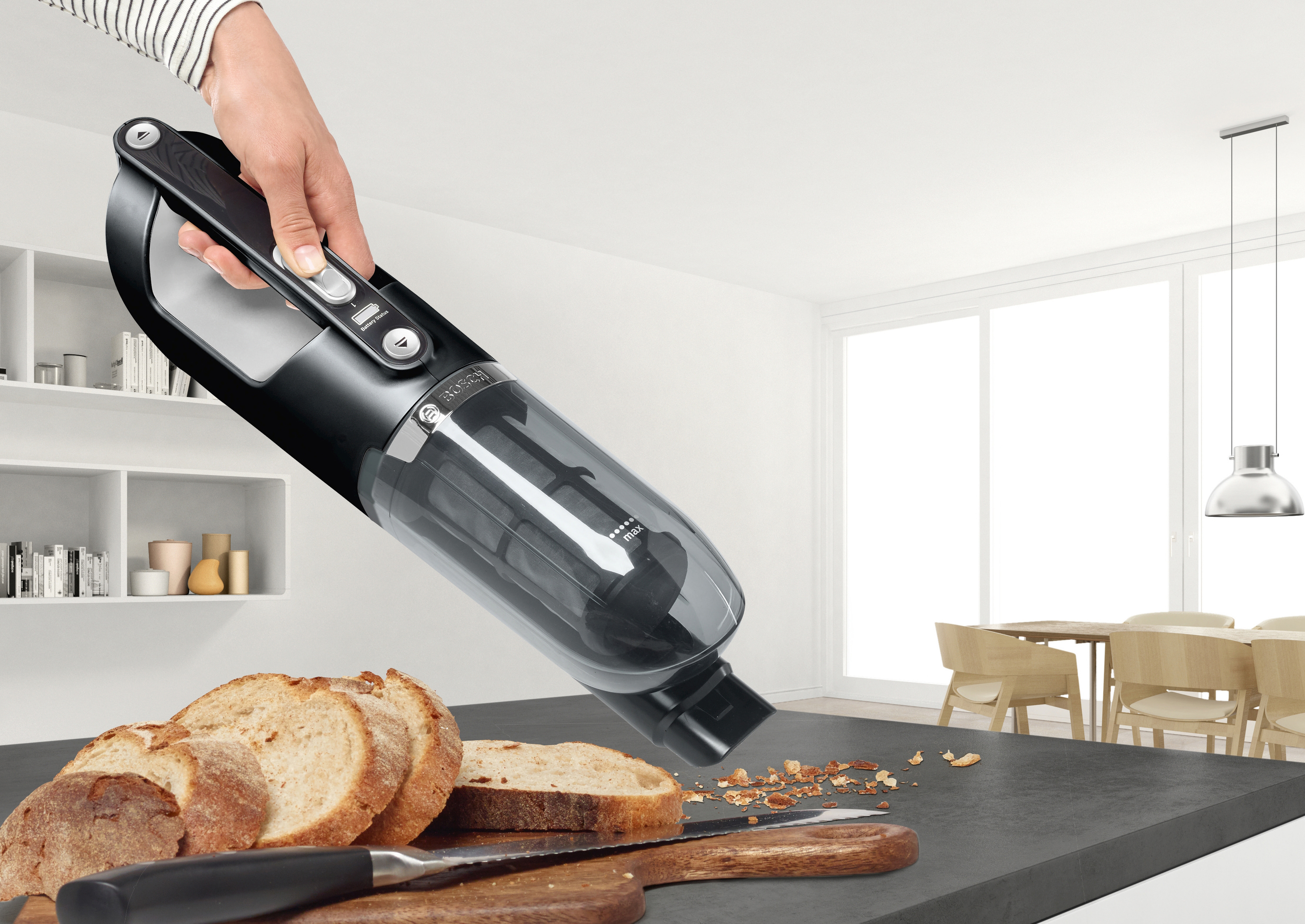 Eine Hand, die einen schwarzen Staubsauger über einem Tresen mit Brot und Krümeln hält.