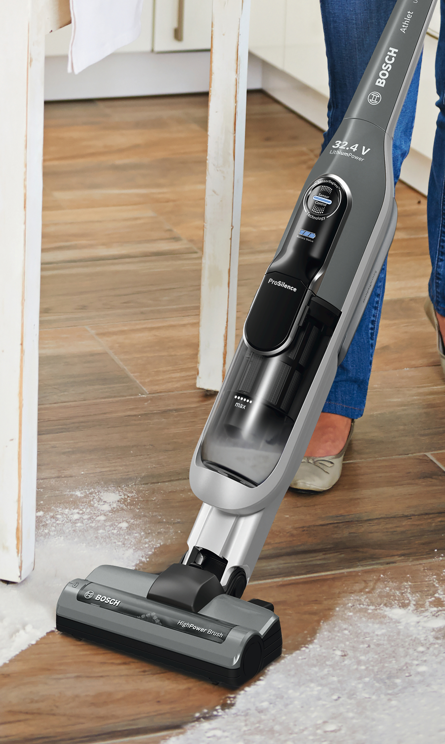 Eine Person benutzt einen grau-schwarzen kabellosen Staubsauger auf einem Holzboden. Weißes Pulver ist sichtbar.