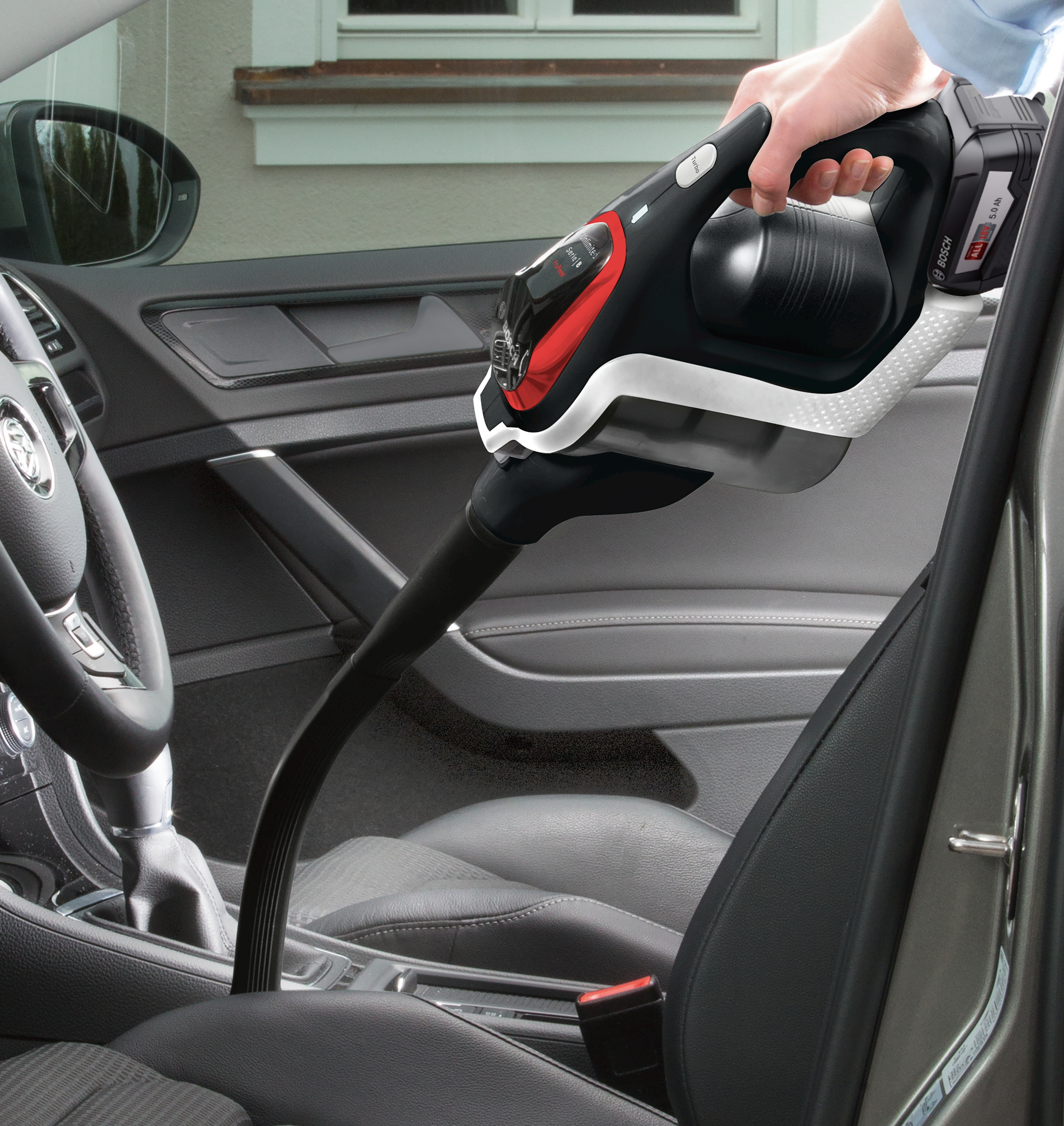 Ein schwarzer und roter Handstaubsauger reinigt das Innere eines Autos.