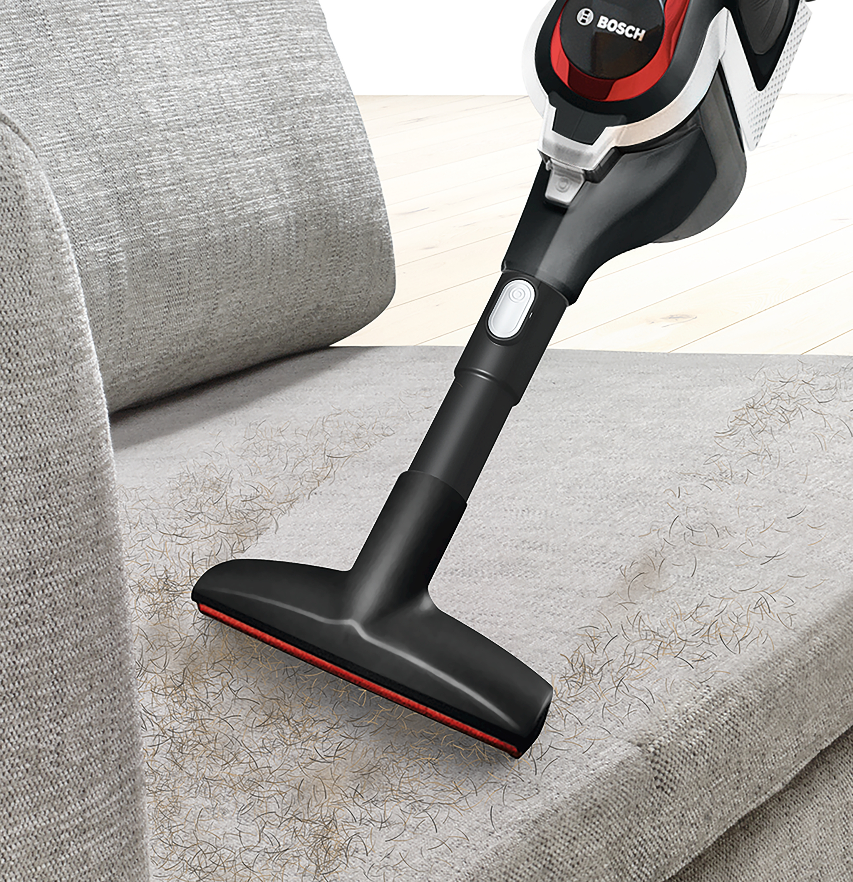 Bosch Staubsauger reinigt graues Sofa. Der Saugkopf entfernt Haare und Schmutz.