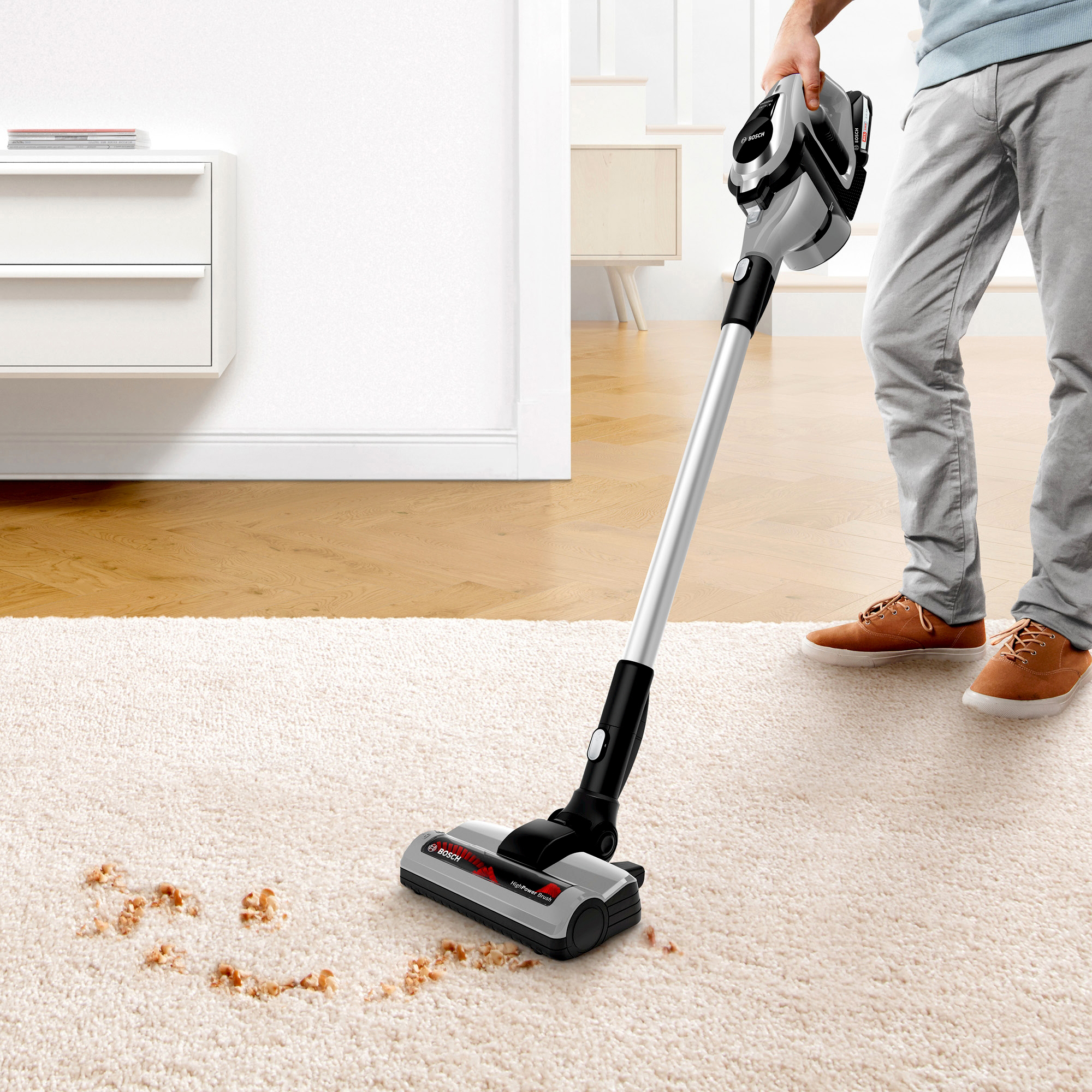 Mann, der einen Teppich mit einem kabellosen Bosch-Staubsauger saugt.