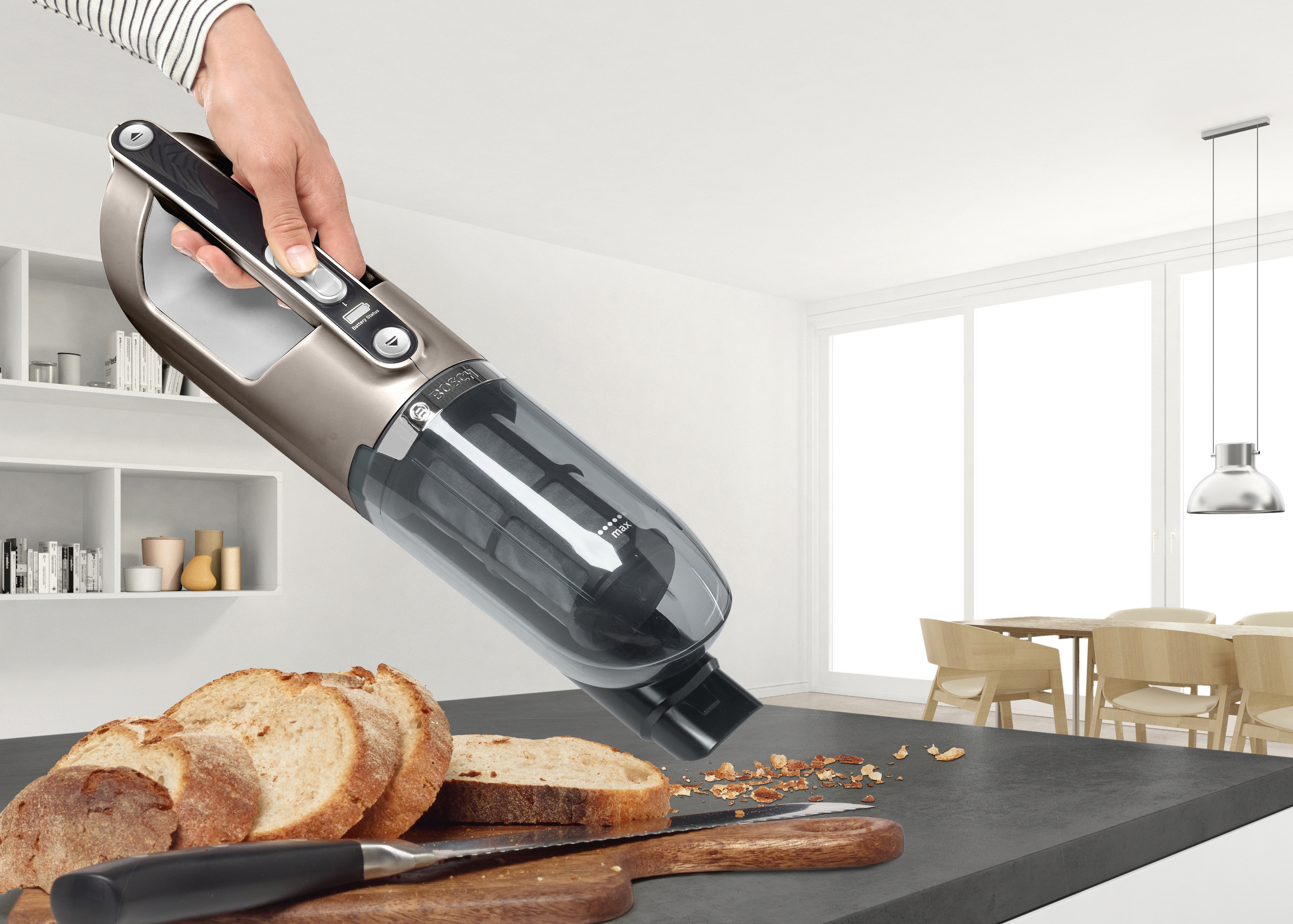Eine Person benutzt einen Handstaubsauger auf einer Küchentheke mit Brot und Krümeln.