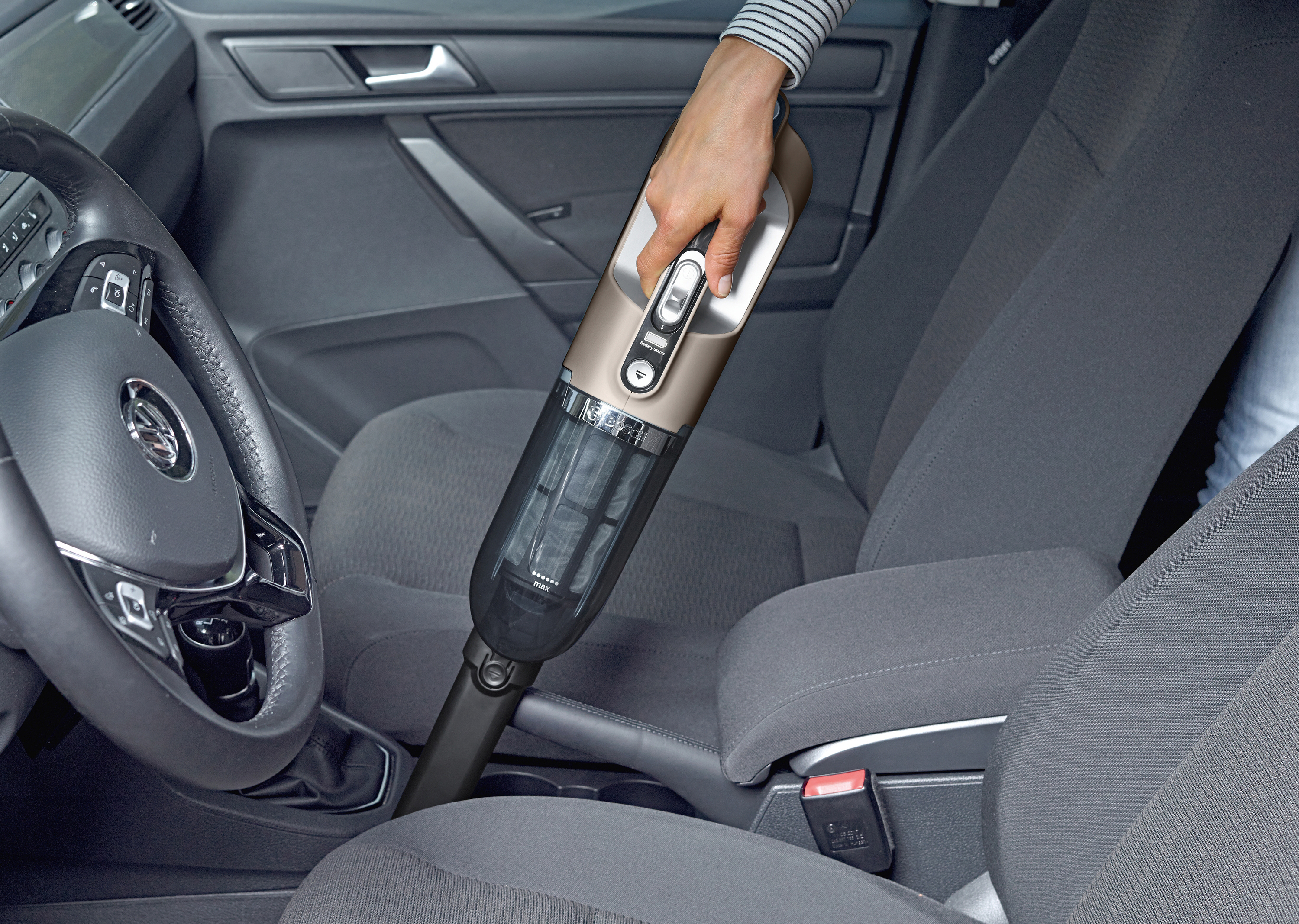 Eine Person saugt einen Autoinnenraum mit einem Handstaubsauger. Das Auto ist grau.