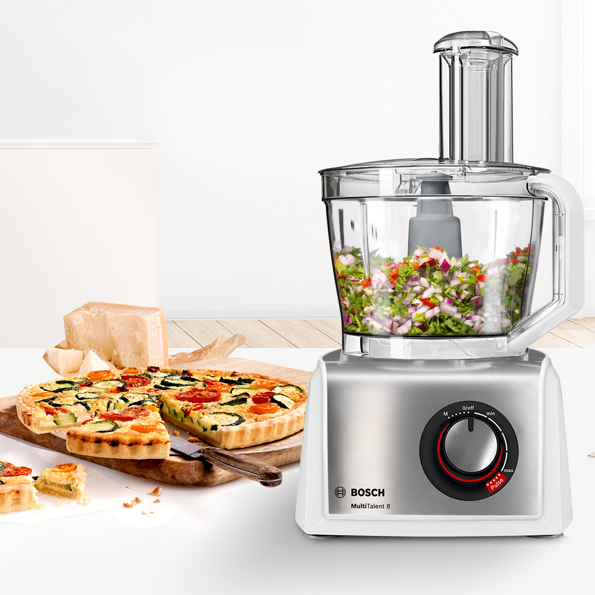 Bosch Küchenmaschine mit gehacktem Gemüse, Pizza und Tarte auf Holztisch.