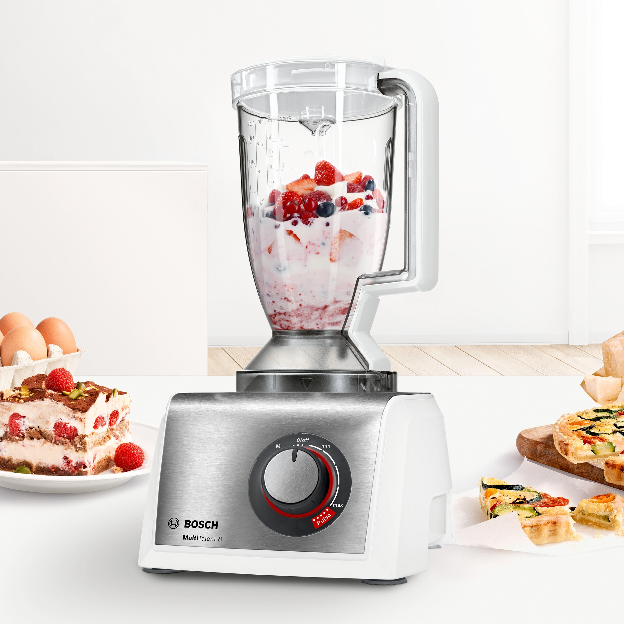 Mixer mit Früchten und Zutaten auf der Küchentheke. Kuchen und Eier sind in der Nähe.