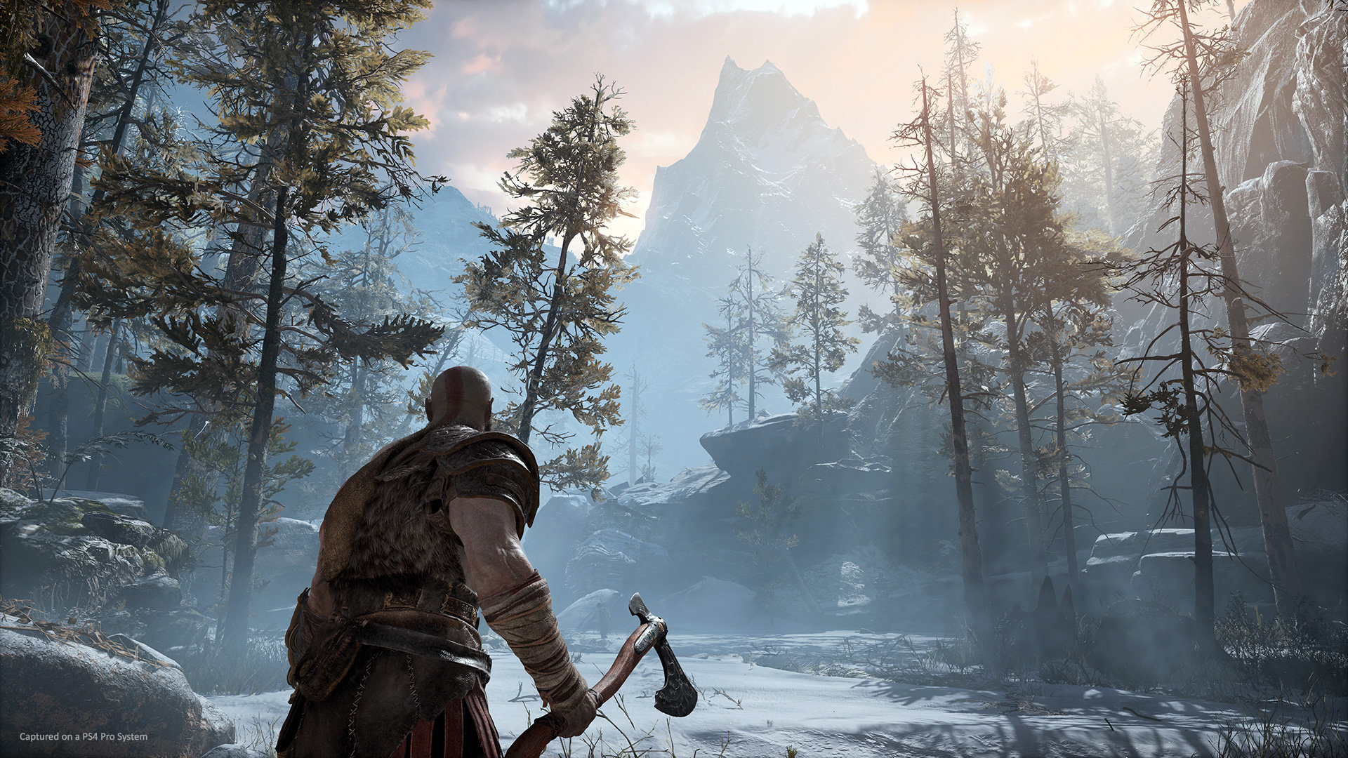 Una escena de videojuego con un hombre sosteniendo un hacha en un bosque nevado con montañas.