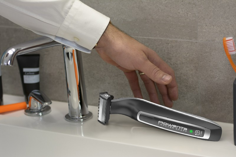 Mano de hombre alcanzando una afeitadora Rowenta Forever Sharp en un lavabo, cerca de un grifo.