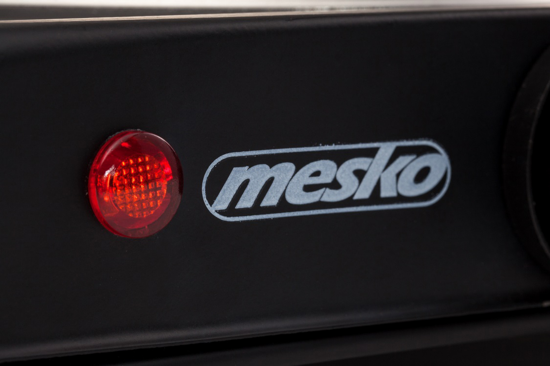 Egy fekete eszköz közeli képe a 'mesko' logóval. Piros lámpa világít balra.