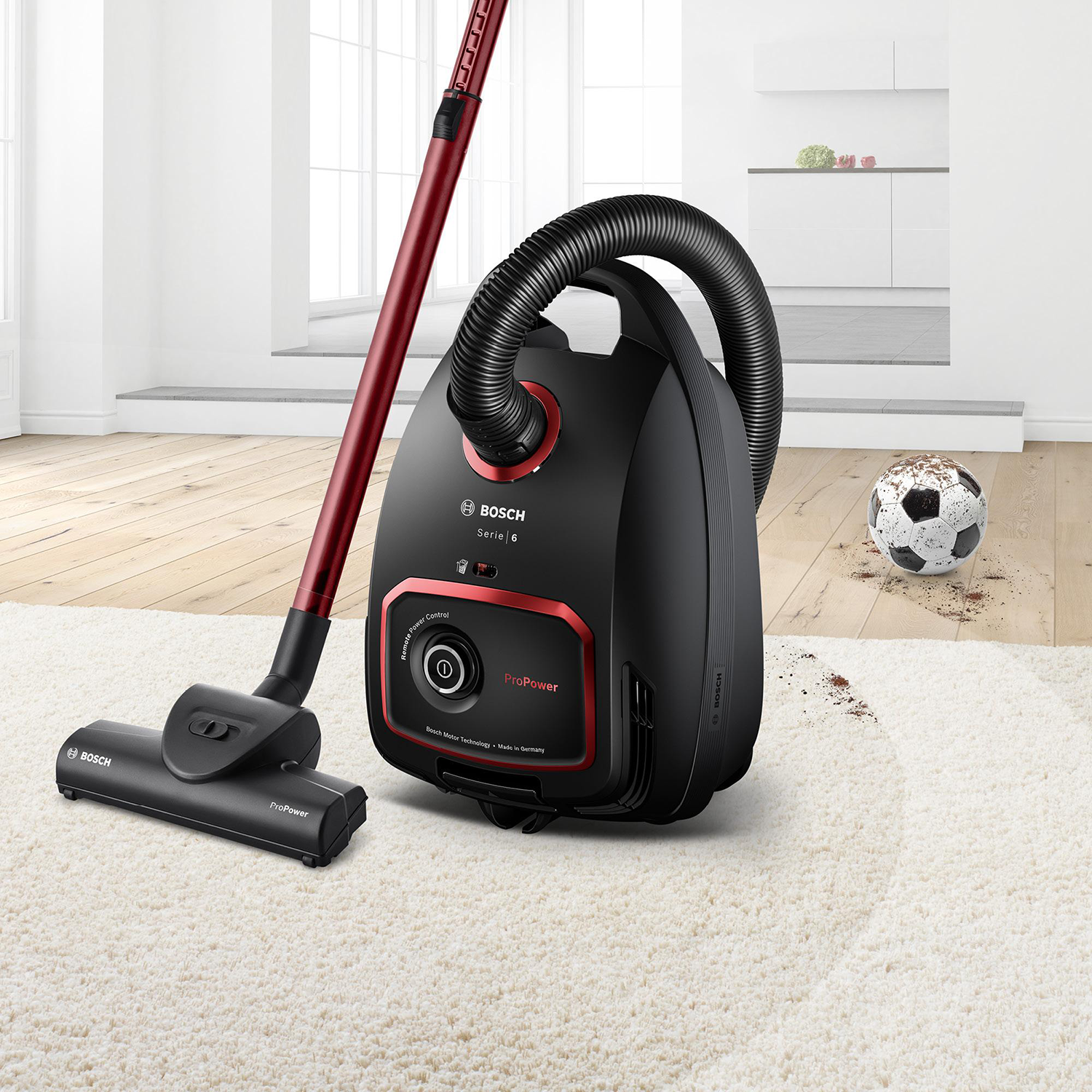 Black Bosch vacuum cleaner with a red handle and nozzle.  A soccer ball is on the floor.