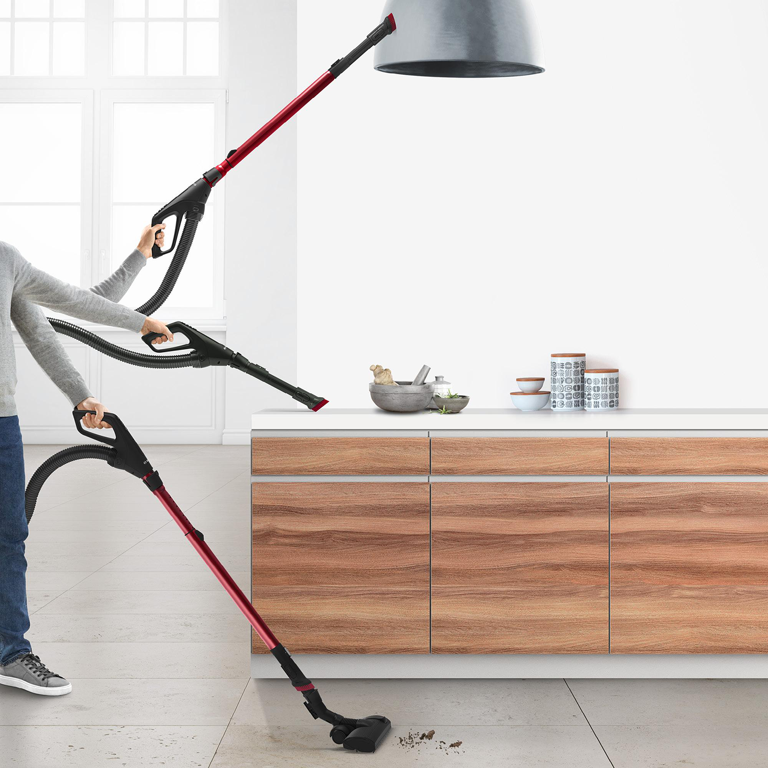 A person using a vacuum cleaner in a kitchen with wooden cabinets and a white wall.