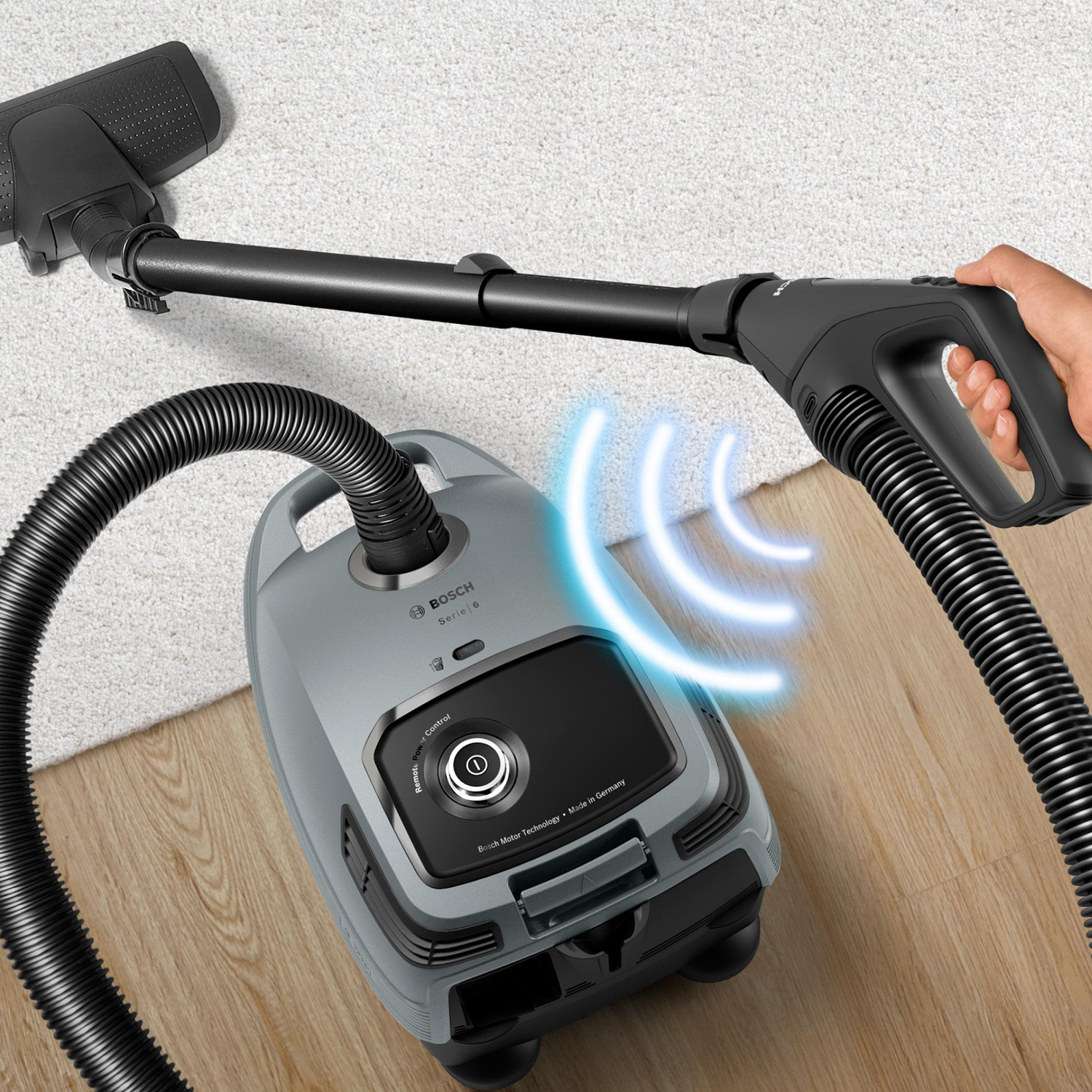 A gray vacuum cleaner on a carpet. A hand is holding the hose.