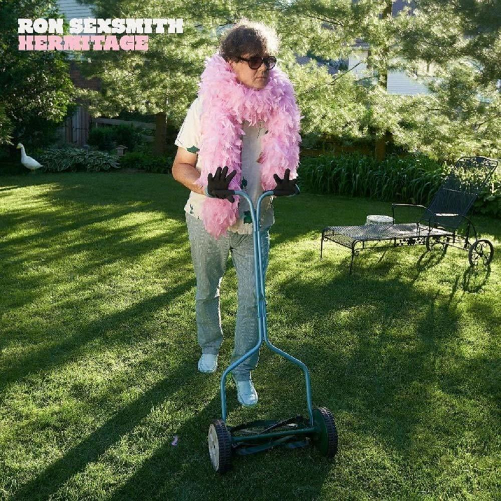 Mann mit pinker Federboa mäht Rasen mit Handrasenmäher. Grünes Gras, Bäume im Hintergrund.