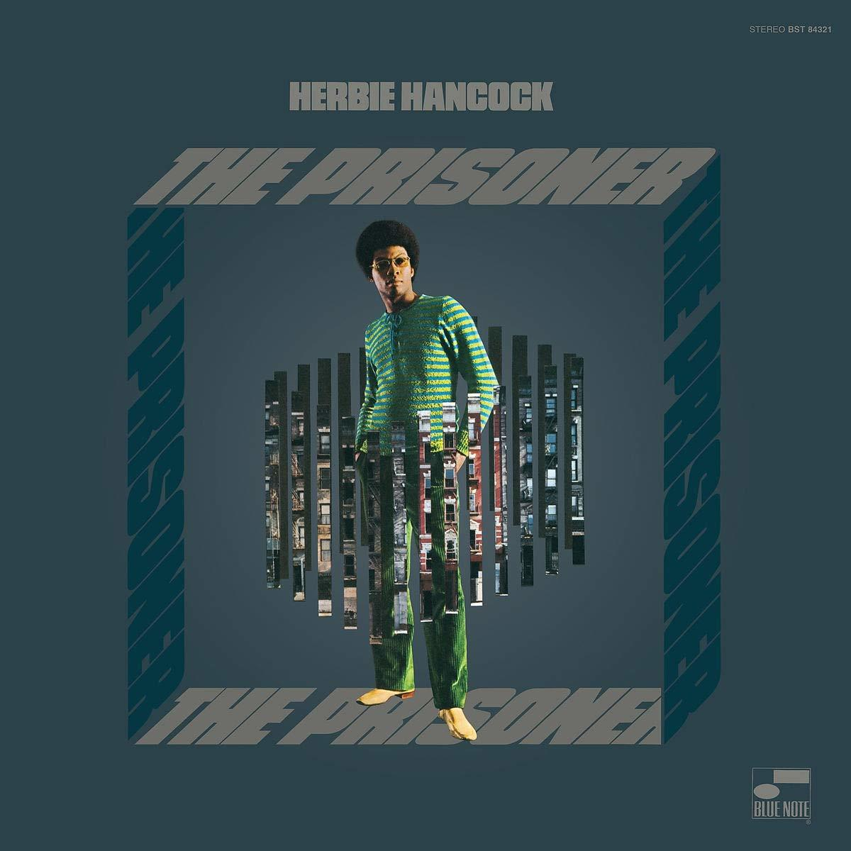 Herbie Hancock, The Prisoner album borítója. Zöld ruhás férfi, napszemüveg. Átvágott épületek. Kék háttér.