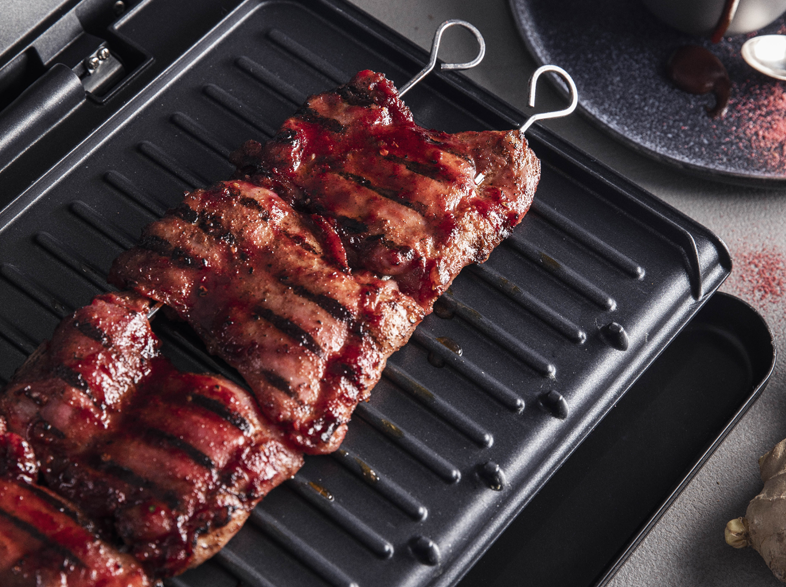 Grillezett hús nyárson fekete grillen, szósszal és tányérral.