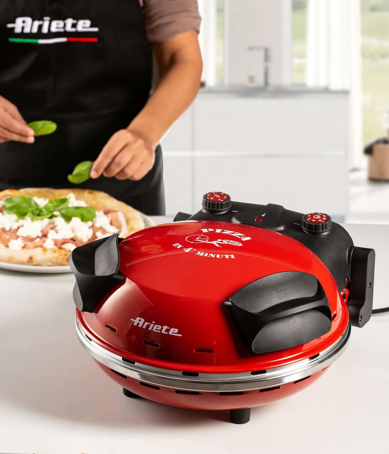 Persona con horno de pizza. Pizza con mozzarella en la mesa. Logo 'Ariete' visible.