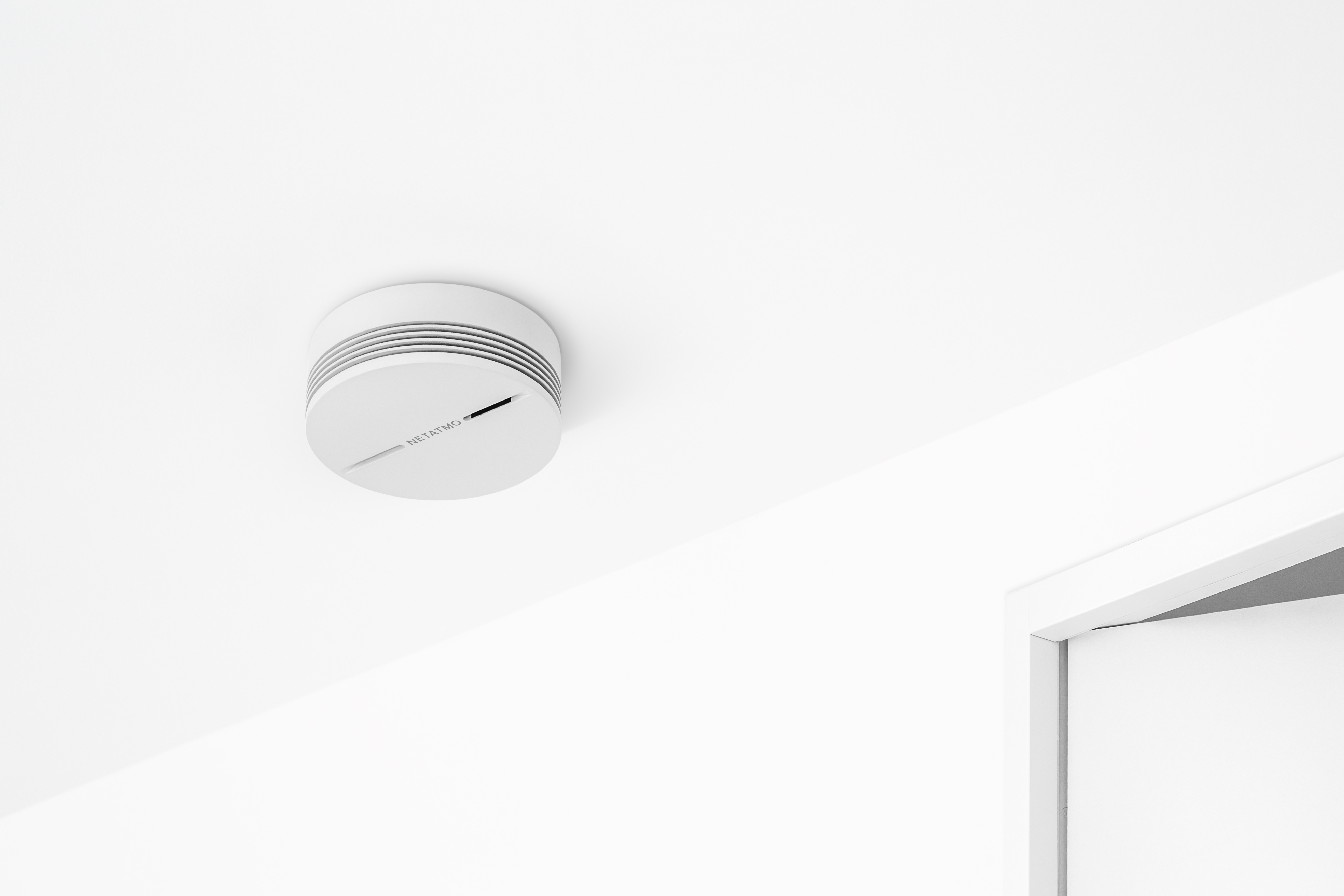 Un rilevatore di fumo bianco è montato su un soffitto bianco, con un telaio della porta bianco visibile.