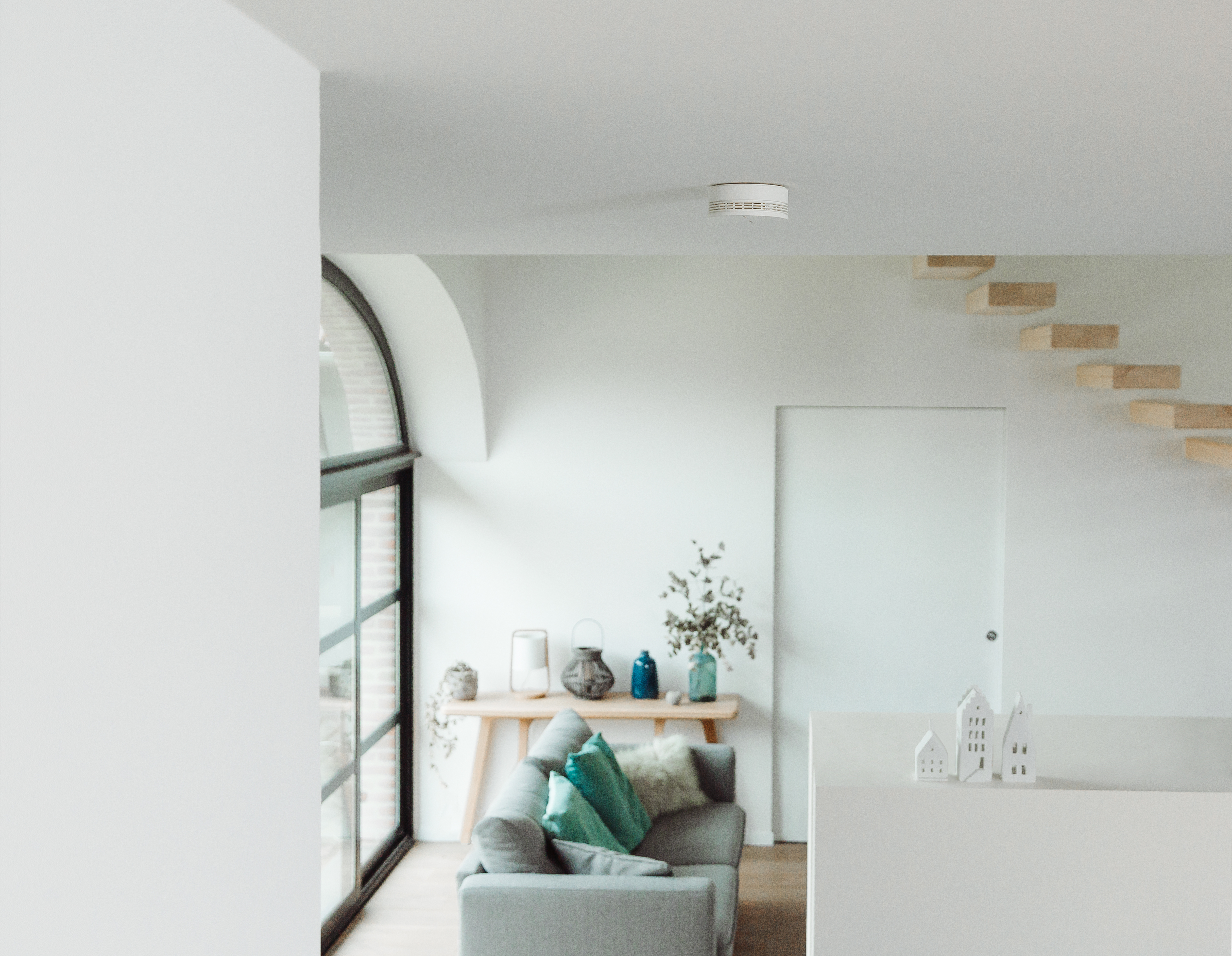 Soggiorno bianco moderno. Un rilevatore di fumo sul soffitto, un divano grigio e un tavolo in legno.