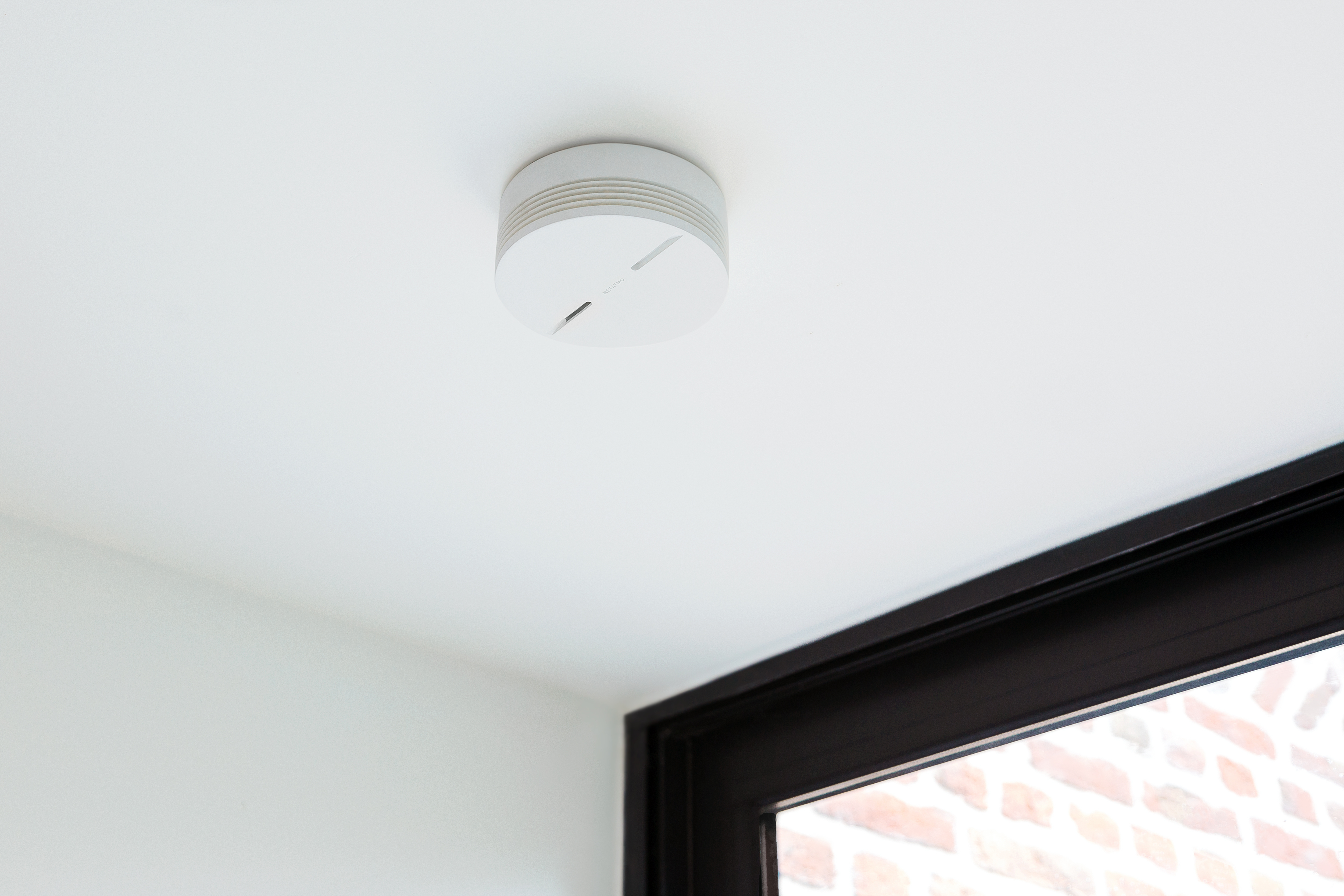 Un rilevatore di fumo bianco montato su un soffitto bianco, visibile in una stanza con cornice nera.