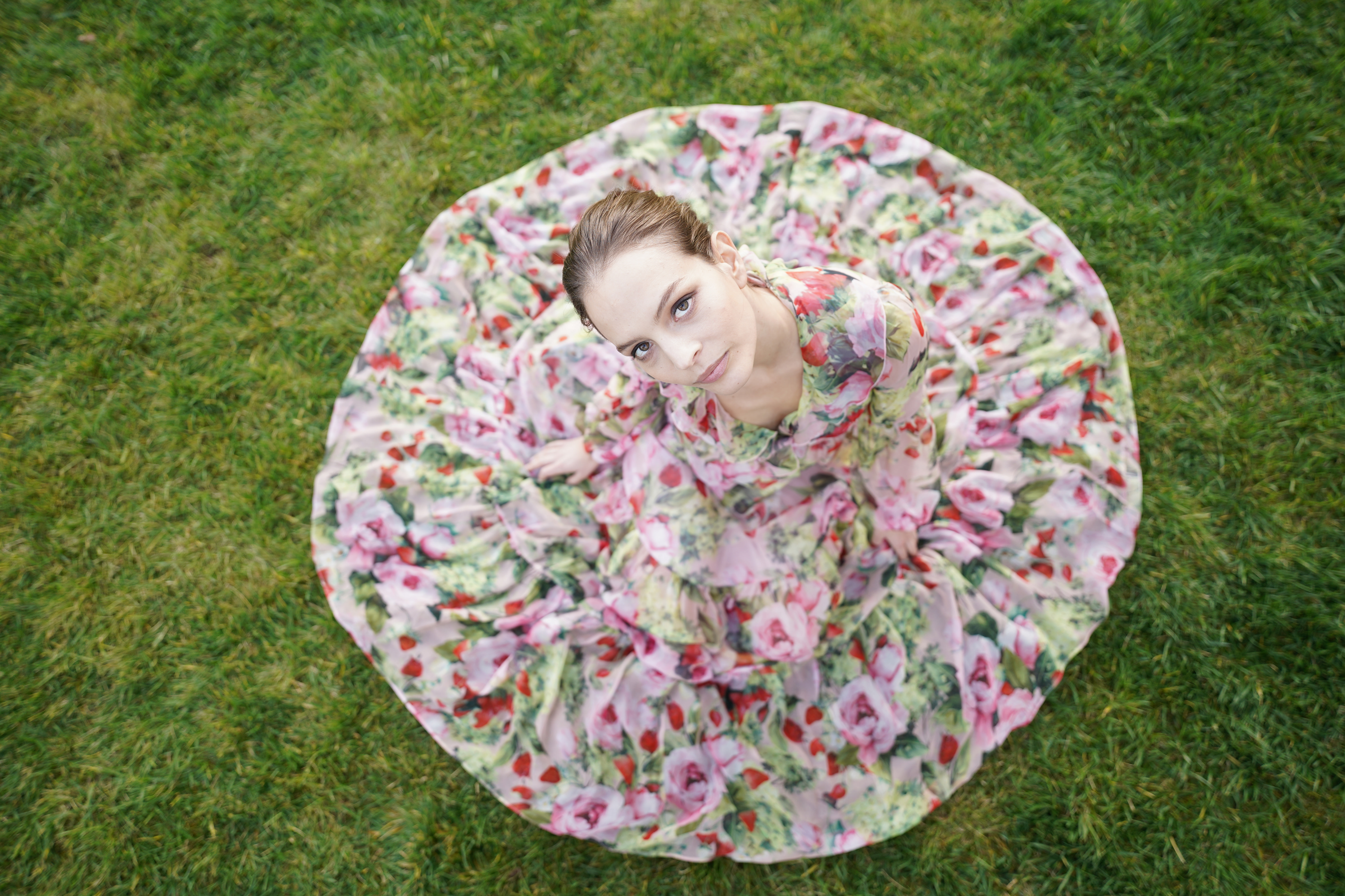 Frau in geblümtem Kleid, blickt nach oben, steht auf Gras.