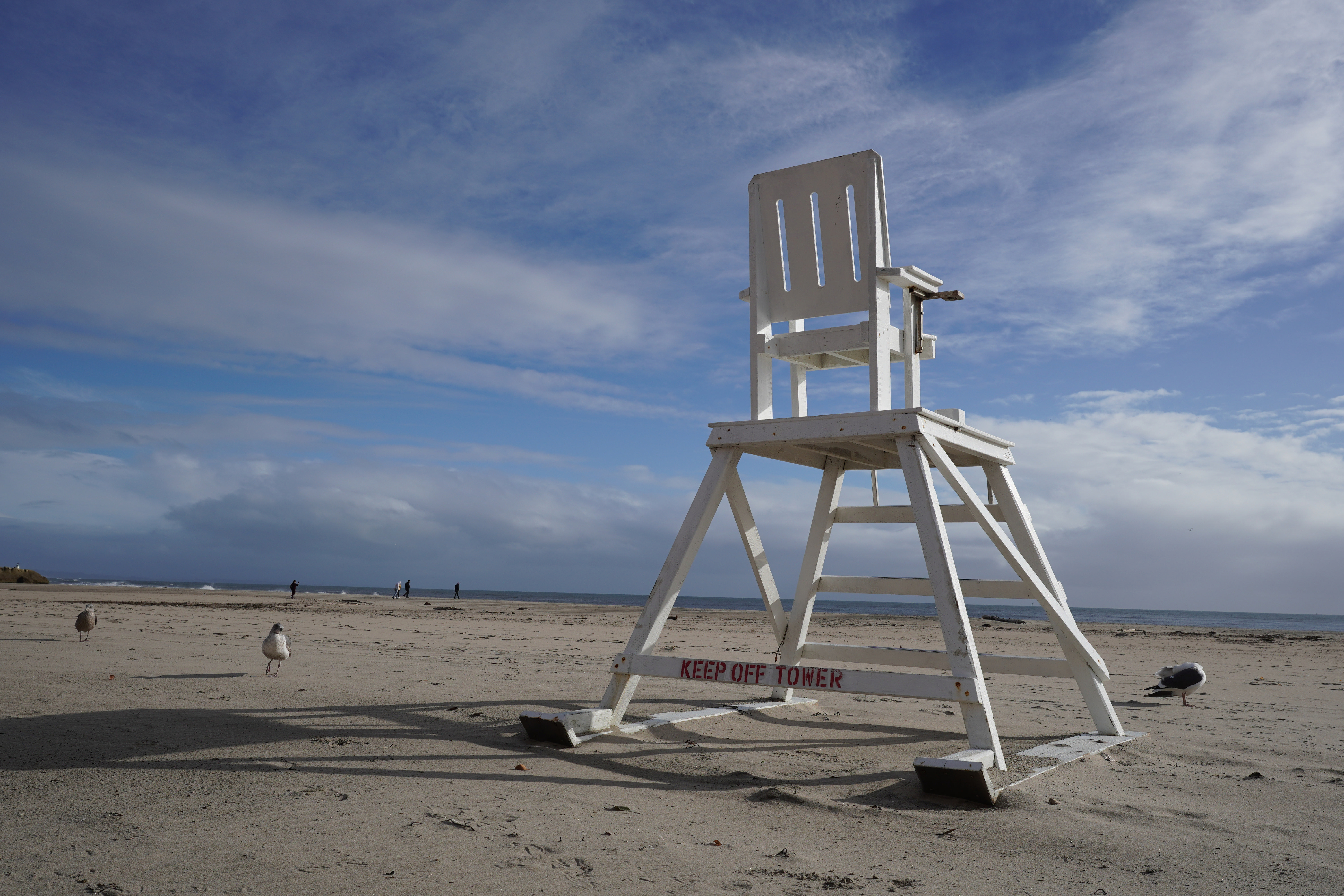 Weißer Rettungsschwimmerstuhl am Sandstrand. Zwei Möwen und blauer Himmel mit Wolken.