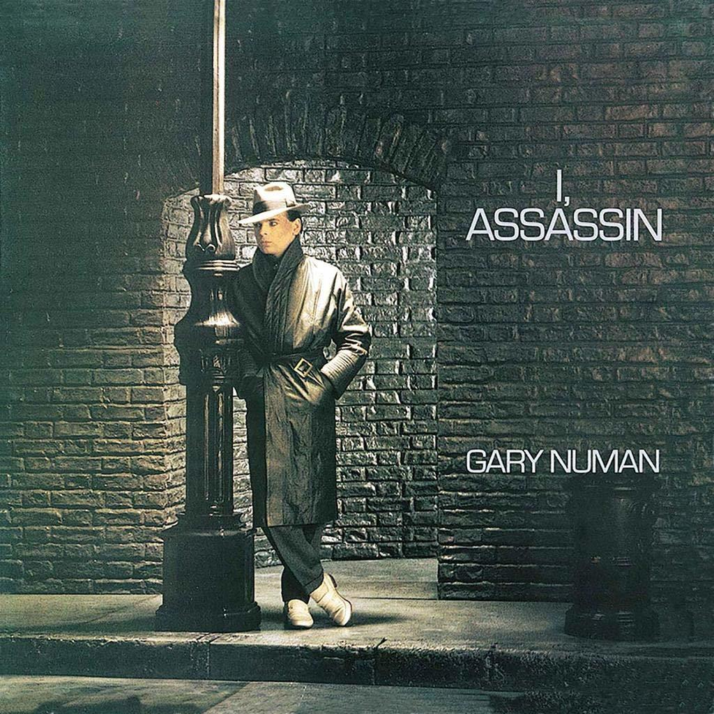 Album-Cover: 'I, Assassin' von Gary Numan. Mann in einem Mantel lehnt an einer Laterne. Hintergrund aus Backstein.