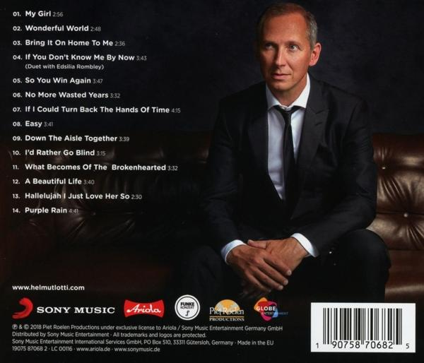Ein Mann im Anzug sitzt auf einer Couch. Albumcover mit Songtiteln im Hintergrund.
