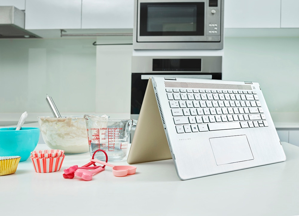 Ein silberner Laptop steht auf einer weißen Theke in einer Küche mit Backutensilien.