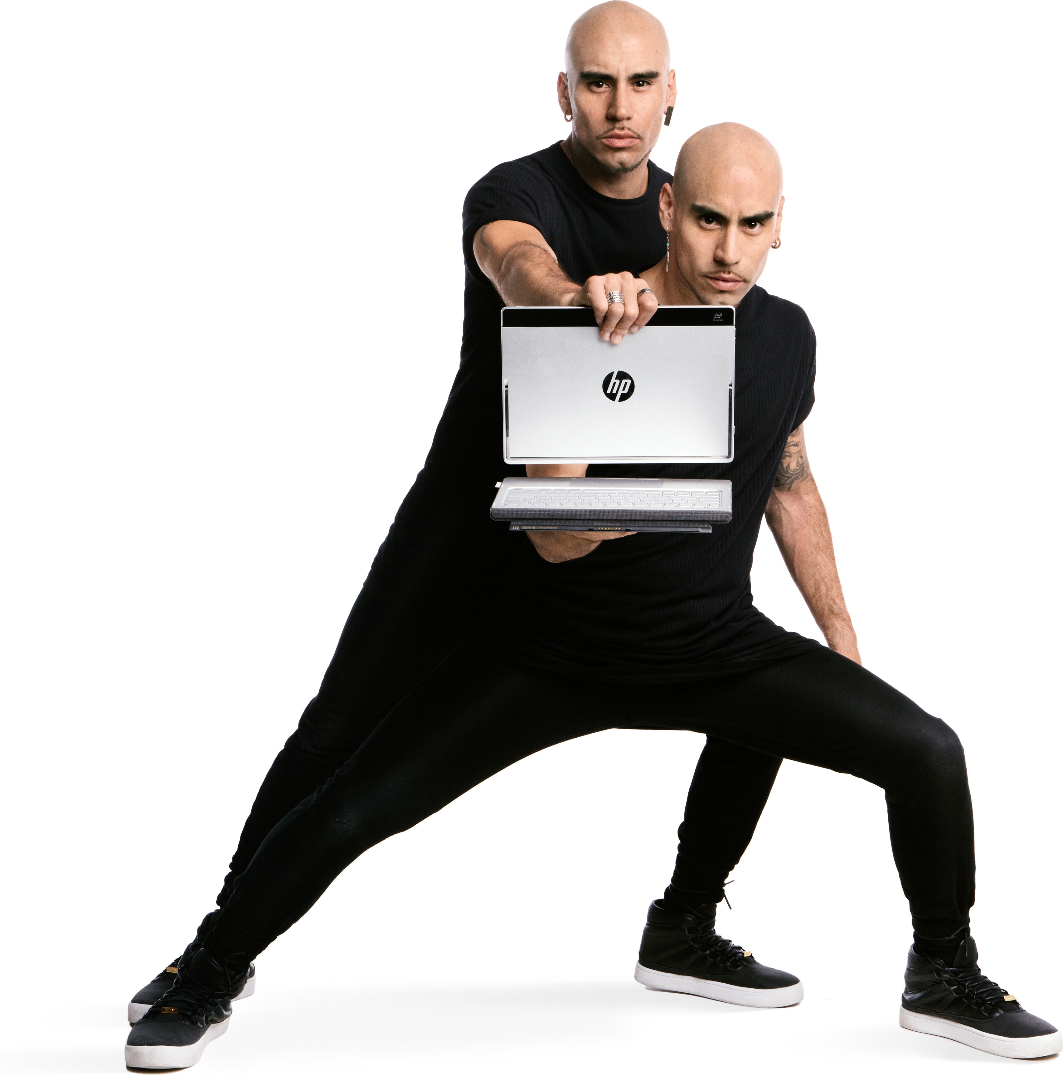 Zwei kahlköpfige Männer in schwarzer Kleidung halten zusammen einen silbernen HP Laptop vor weißem Hintergrund.