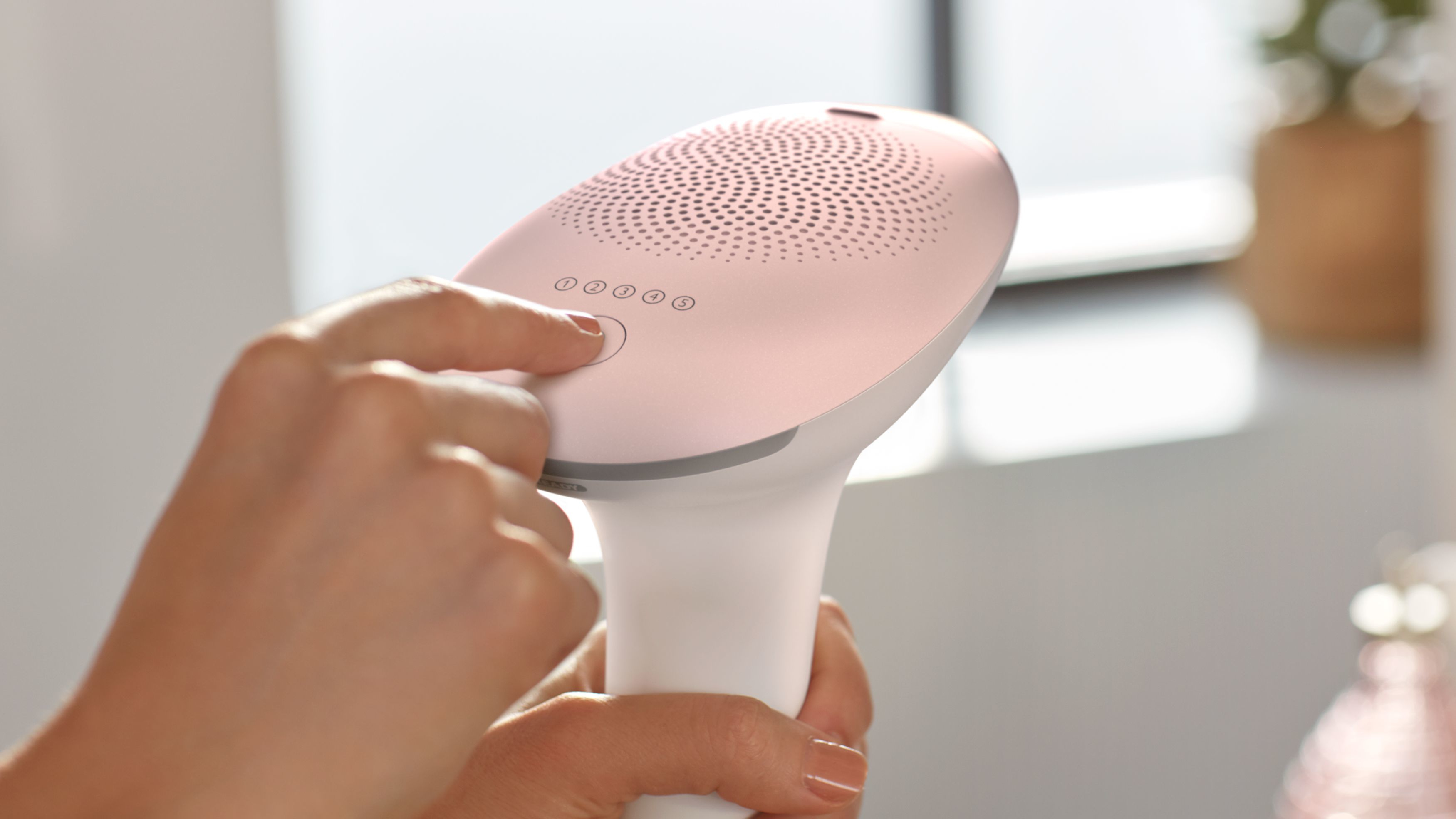 Person pressing a button on a pink hair removal device. White background.
