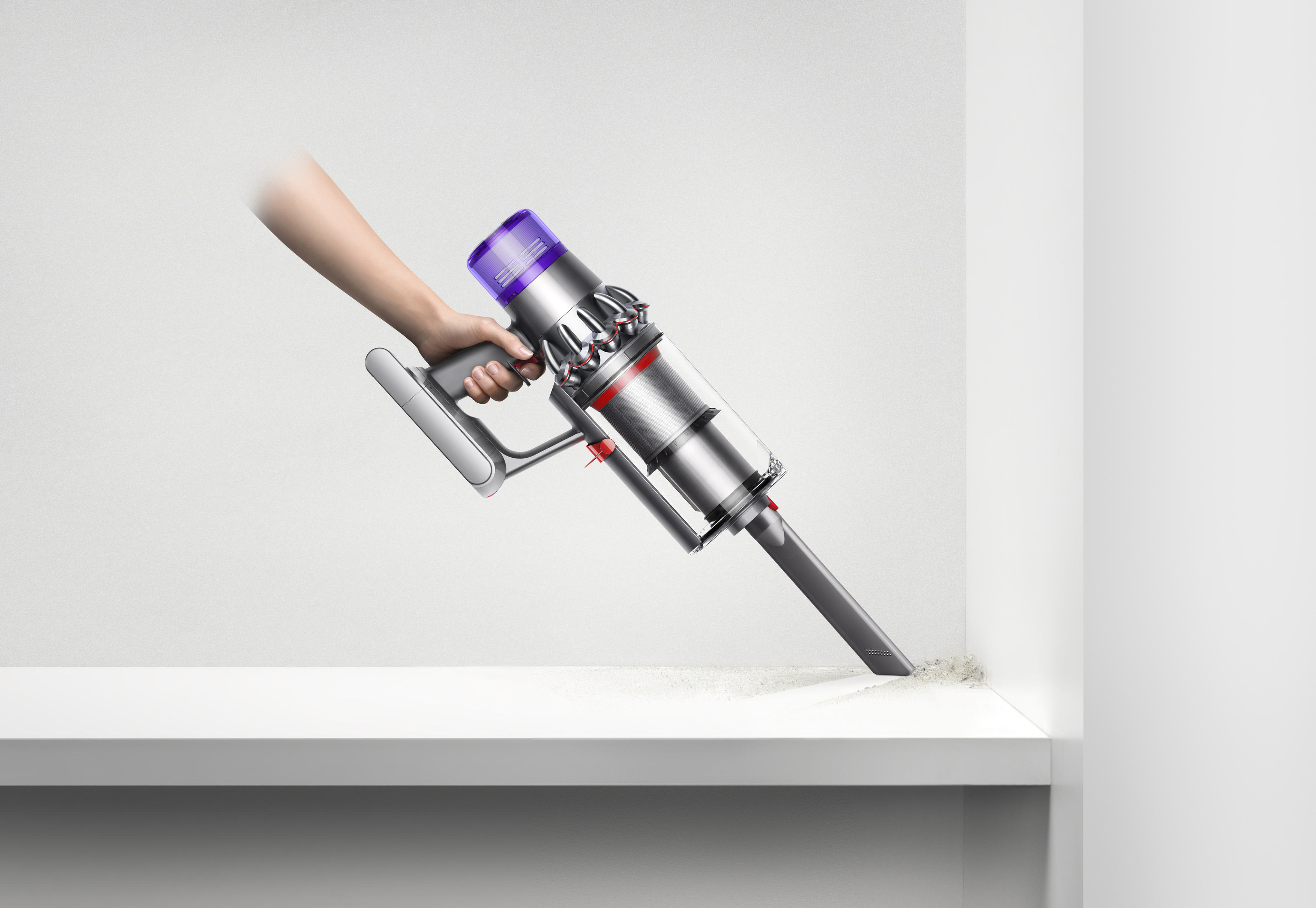 Hand, die einen Dyson-Staubsauger hält und damit ein weißes Regal reinigt.