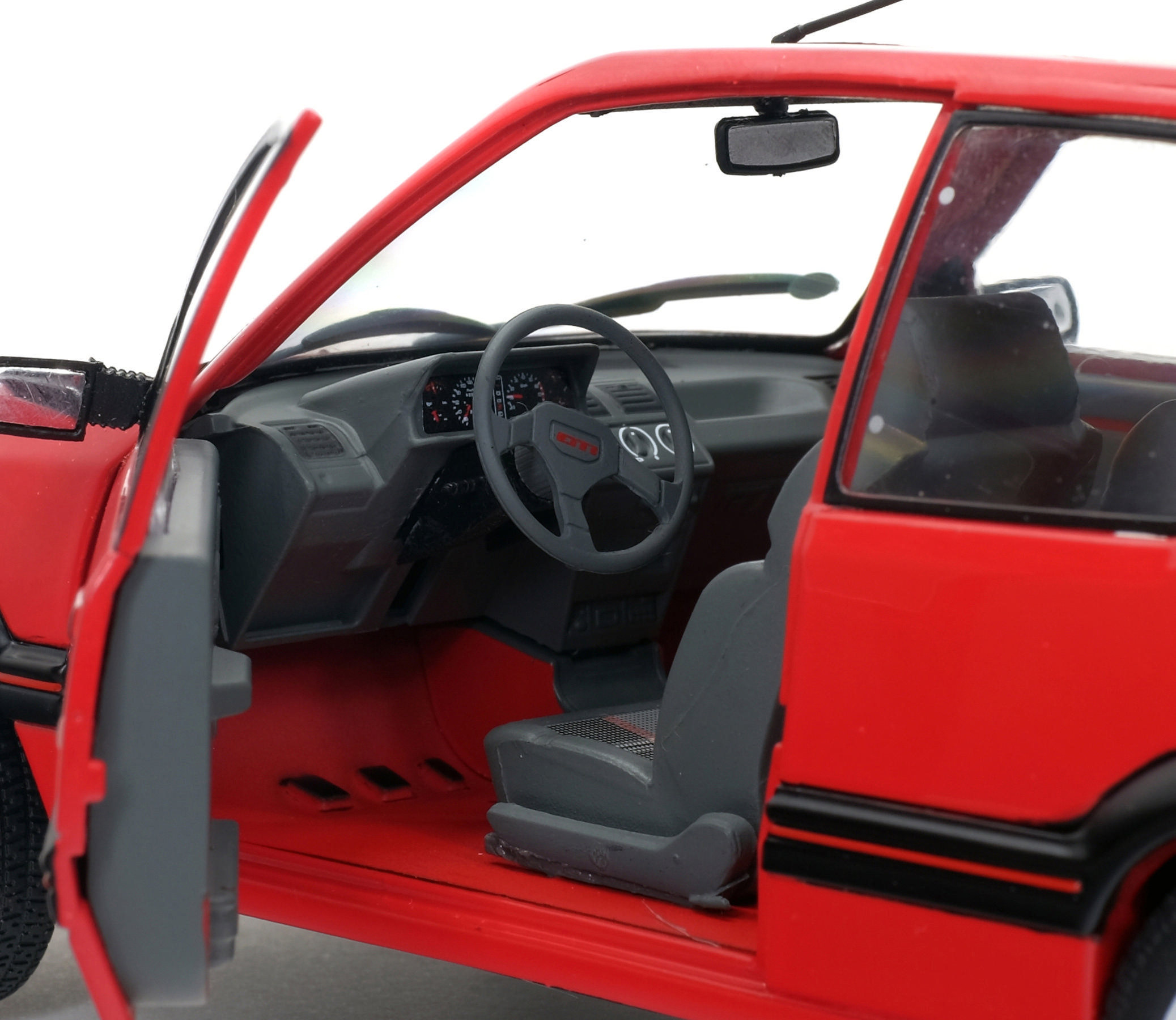 Ein rotes Automodell mit offener Tür zeigt das Innere: Lenkrad, Sitze, Armaturenbrett. Weißer Hintergrund.