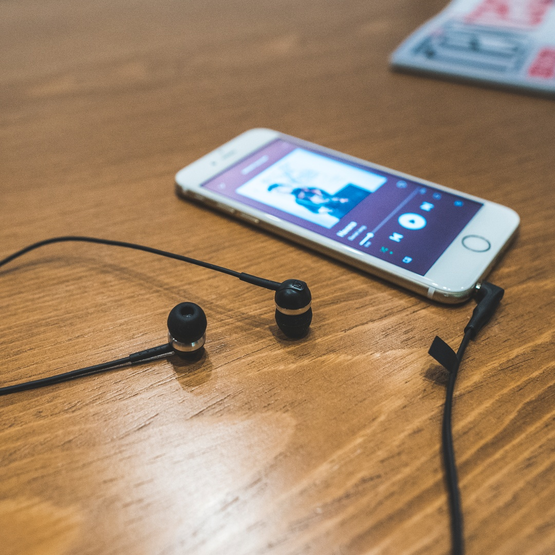Ahşap masada müzik uygulaması ve kablolu kulaklıklarla bir akıllı telefon.