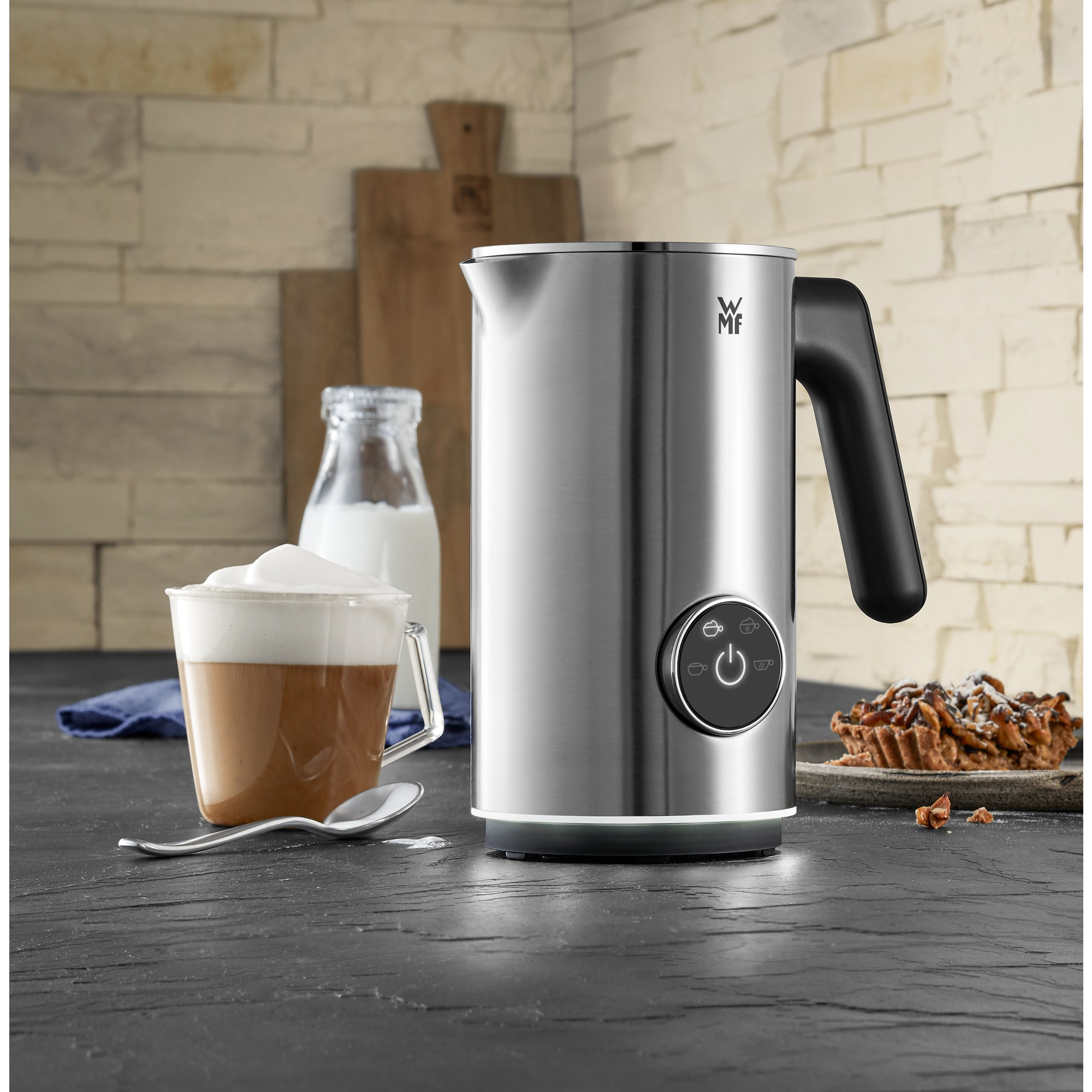 Silver WMF milk frother with a cup of cappuccino, on a black surface.