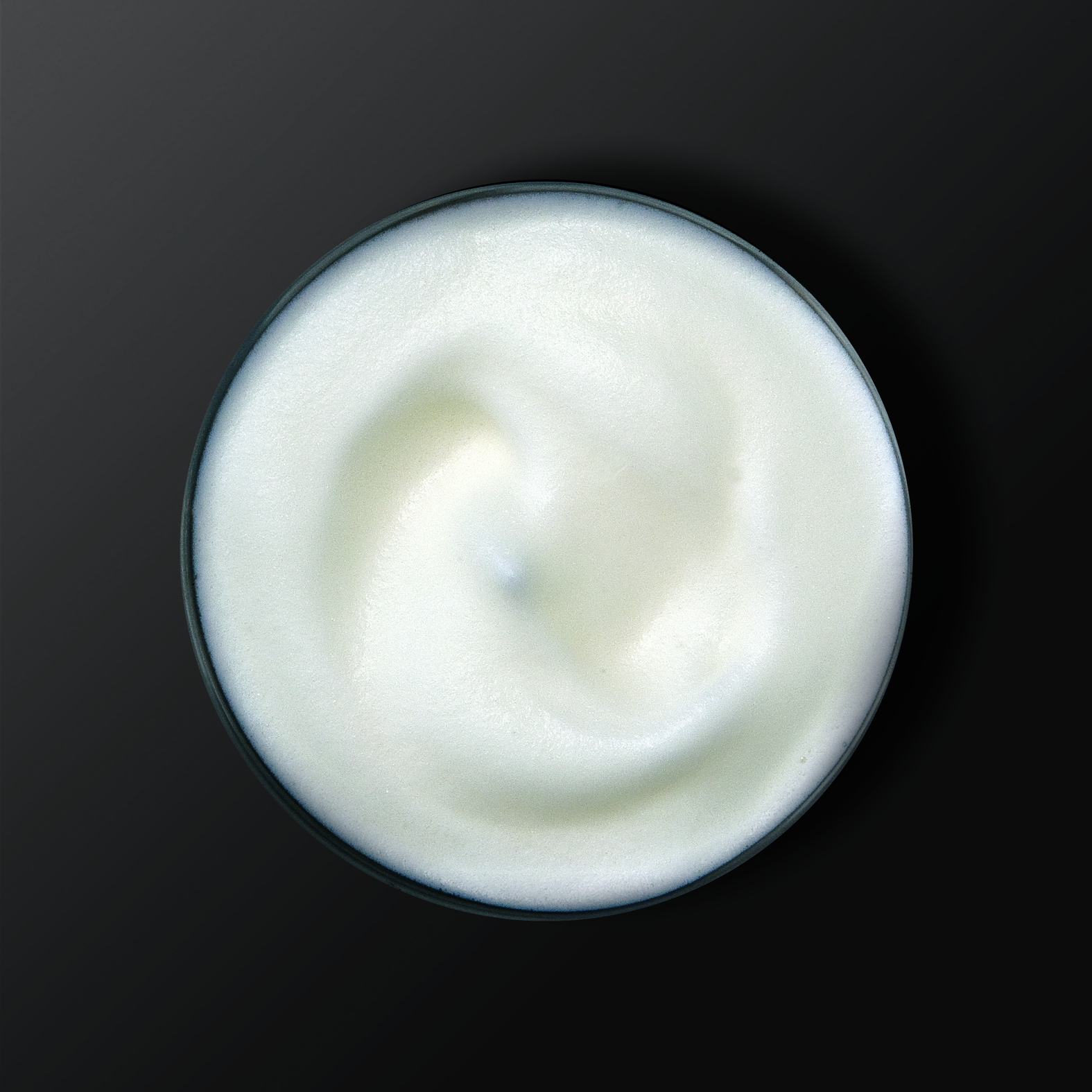 A close-up top view of white, foamy substance in a black bowl against a dark background.