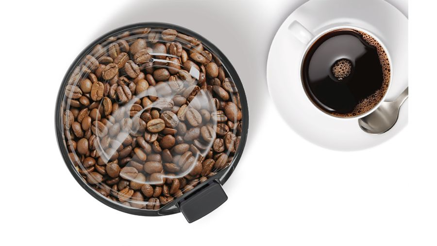 Granos de café en un molinillo junto a una taza de café.